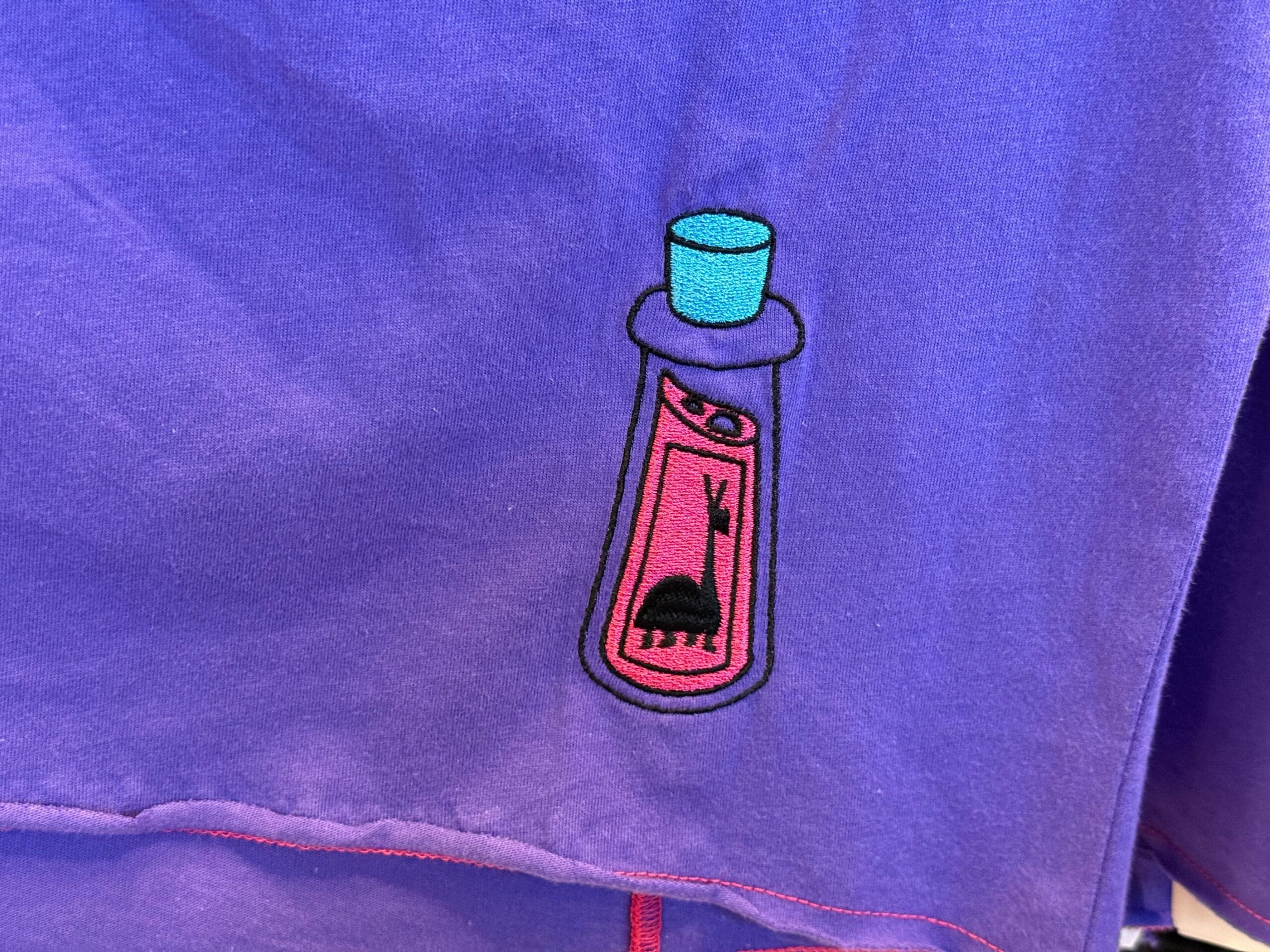 Embroidered pink potion bottle with a turquoise cap and black rabbit inside—perfect for Halloween merchandise.