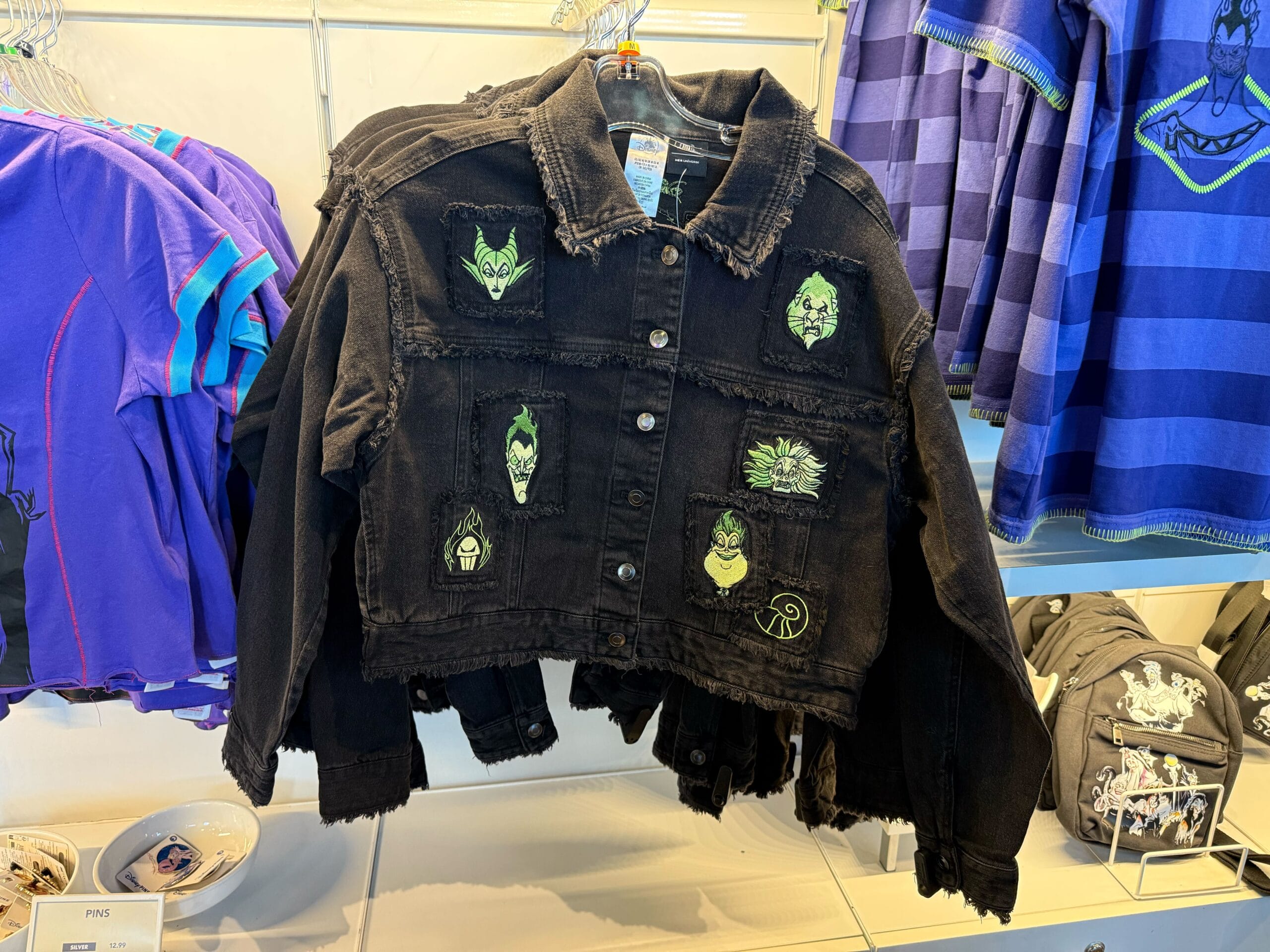 A black denim jacket with Disney villains patches hangs on a store display of Halloween merchandise.