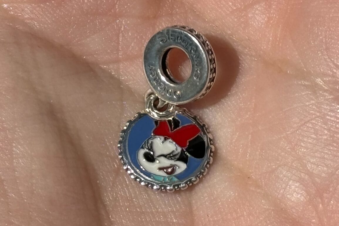A small Minnie Mouse Pandora Charm with a red bow, held in a person's hand.