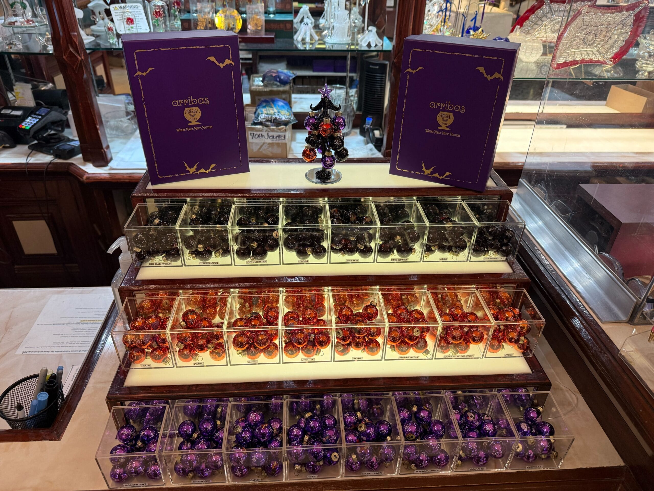 Display of assorted foil-wrapped chocolates in clear bins, with purple Halloween-themed boxes on top.