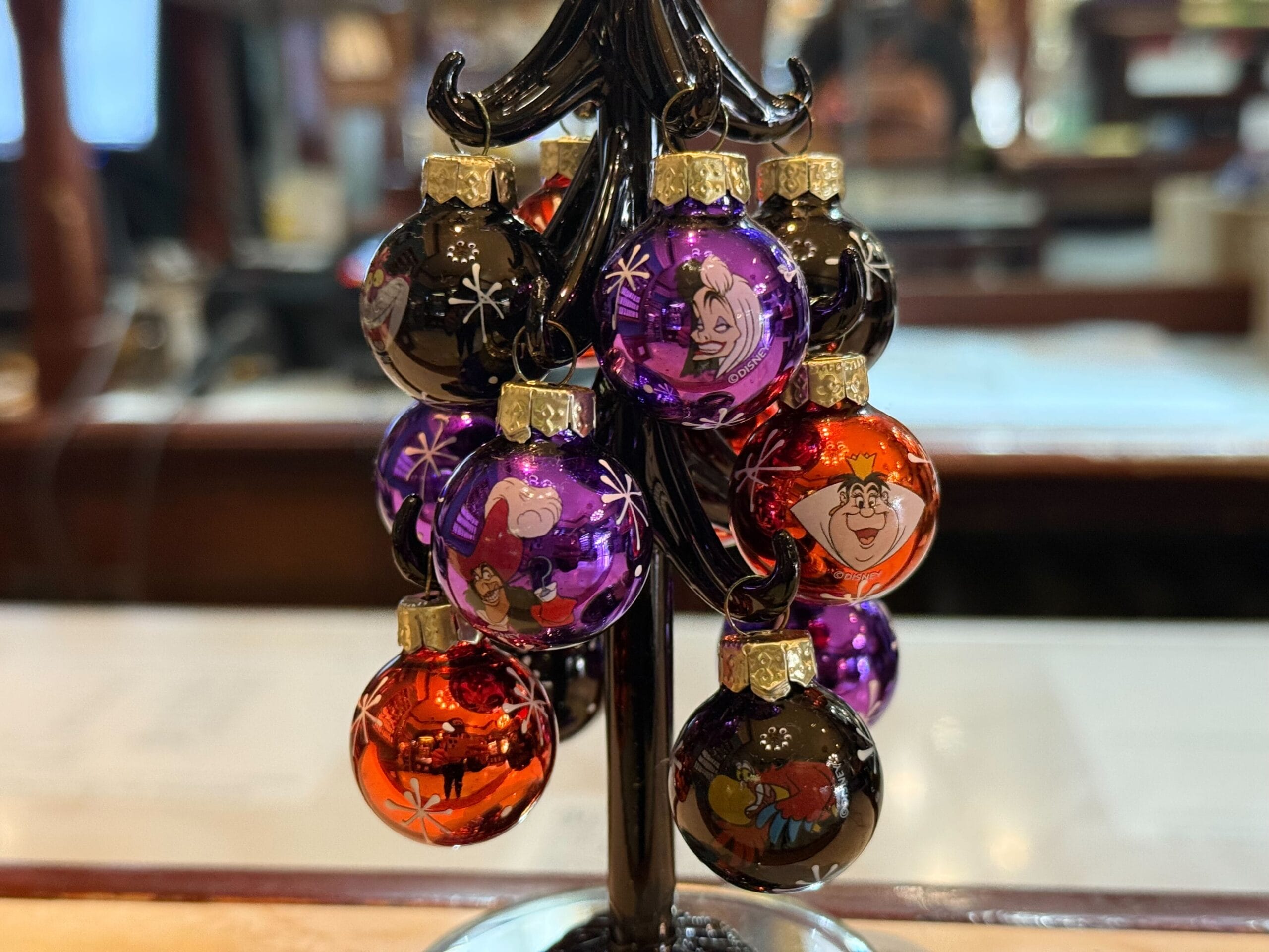 Small purple, red, and black Christmas ornaments with cartoon characters hanging on a black metal tree stand.