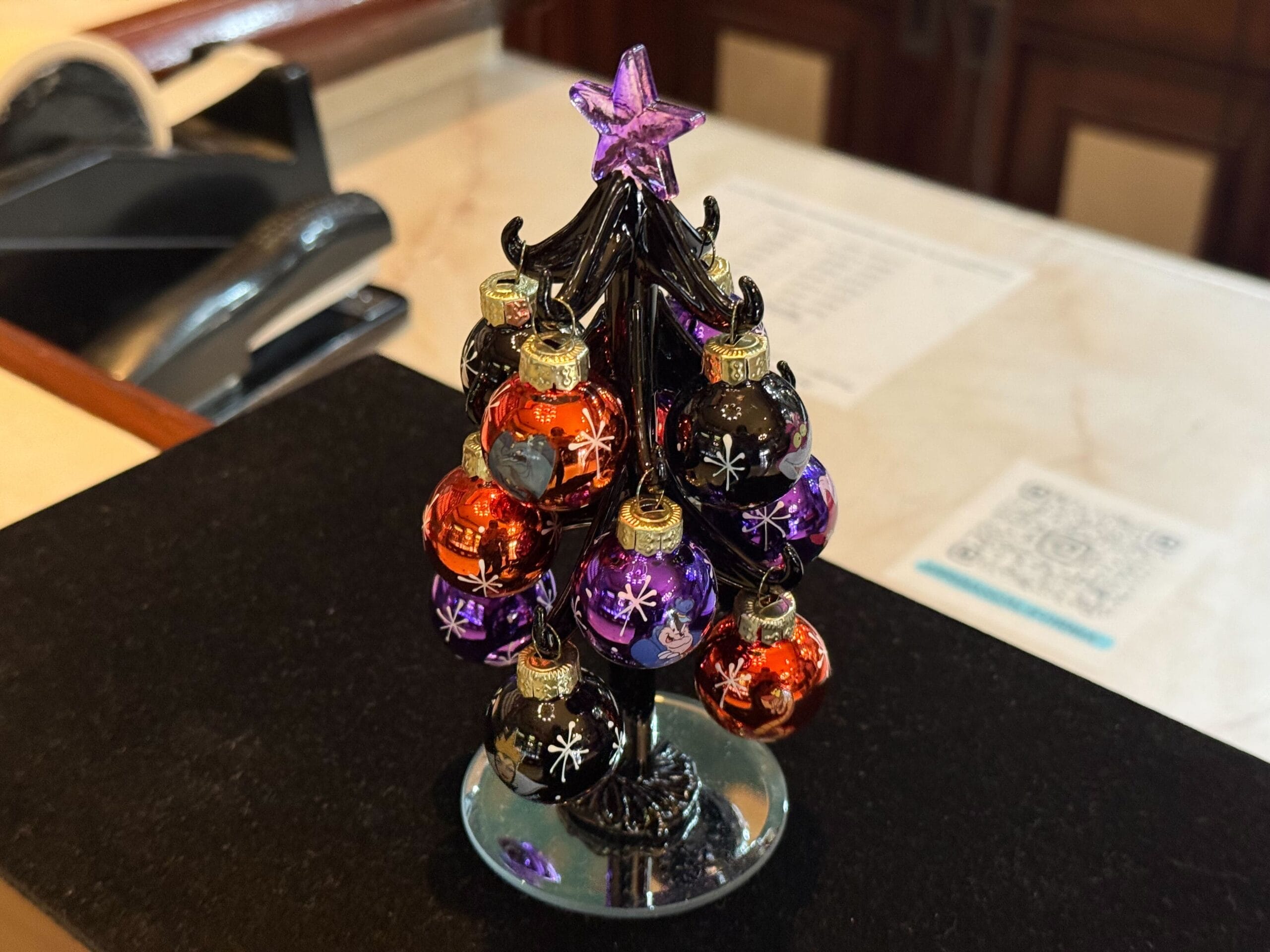 A small glass tree with orange and purple ornaments sits on a counter, topped with a purple star.