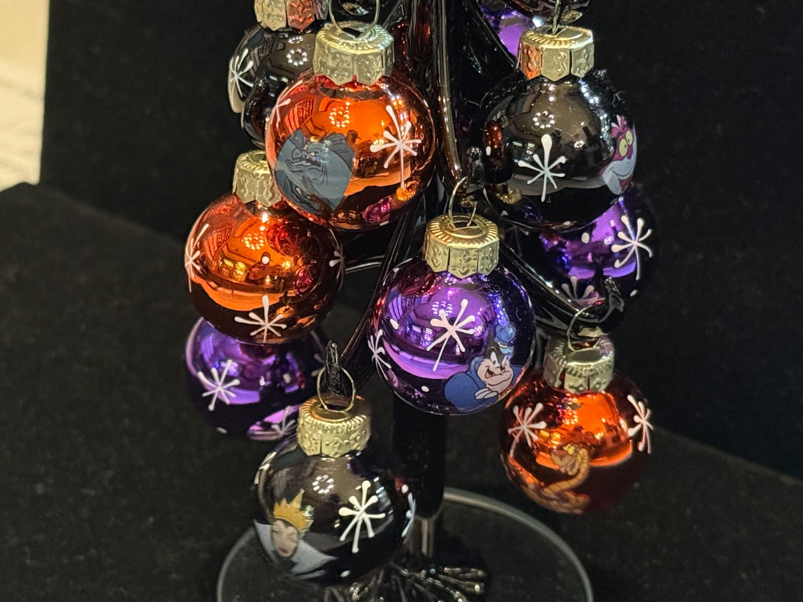 Mini Christmas ornaments featuring Disney villains hang on a small black tree against a dark background.