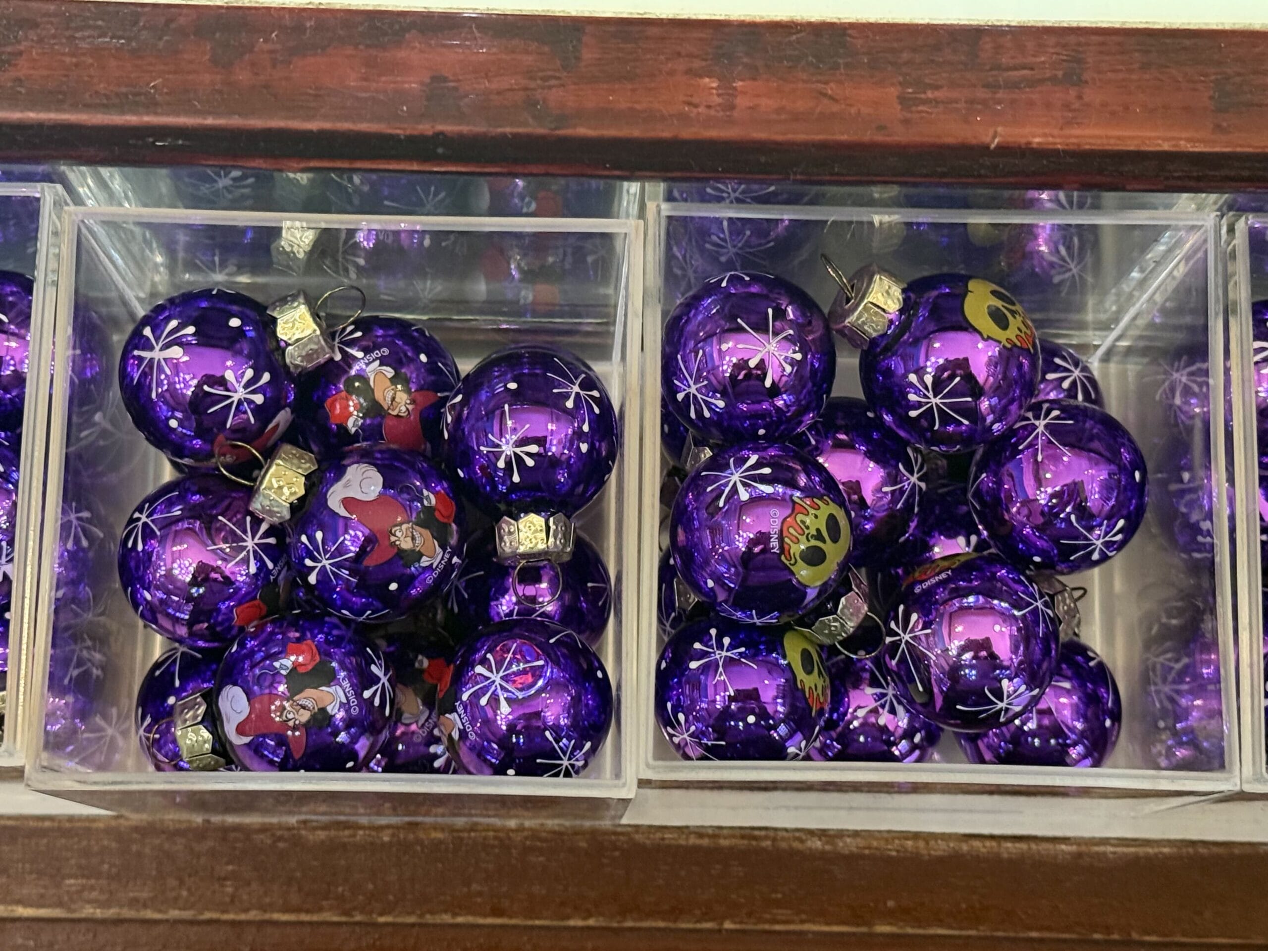 Two clear boxes filled with shiny purple Christmas ornaments decorated with snowflakes and cartoon faces.