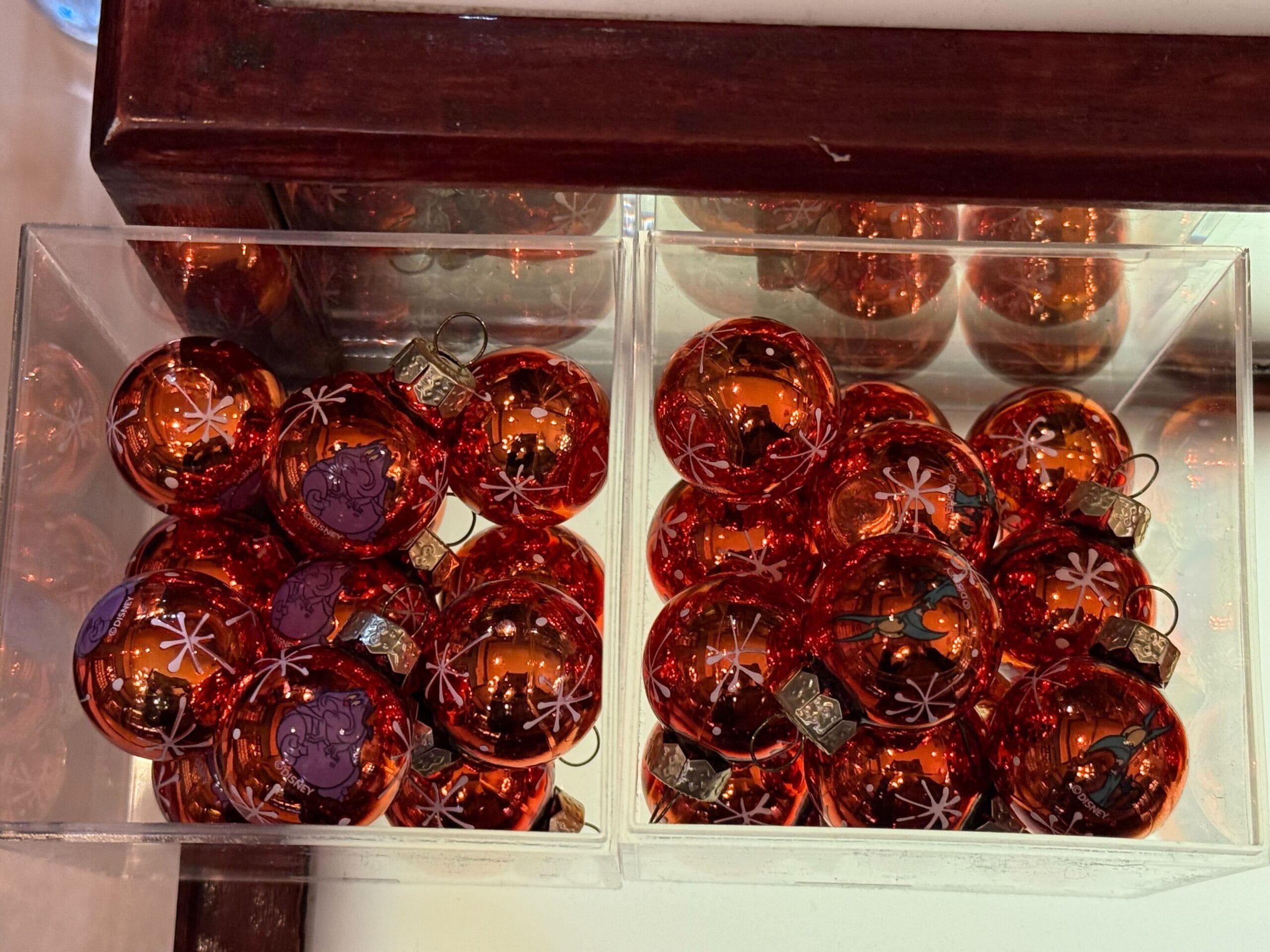 Two clear containers filled with shiny red Christmas ornaments decorated with white snowflake patterns.