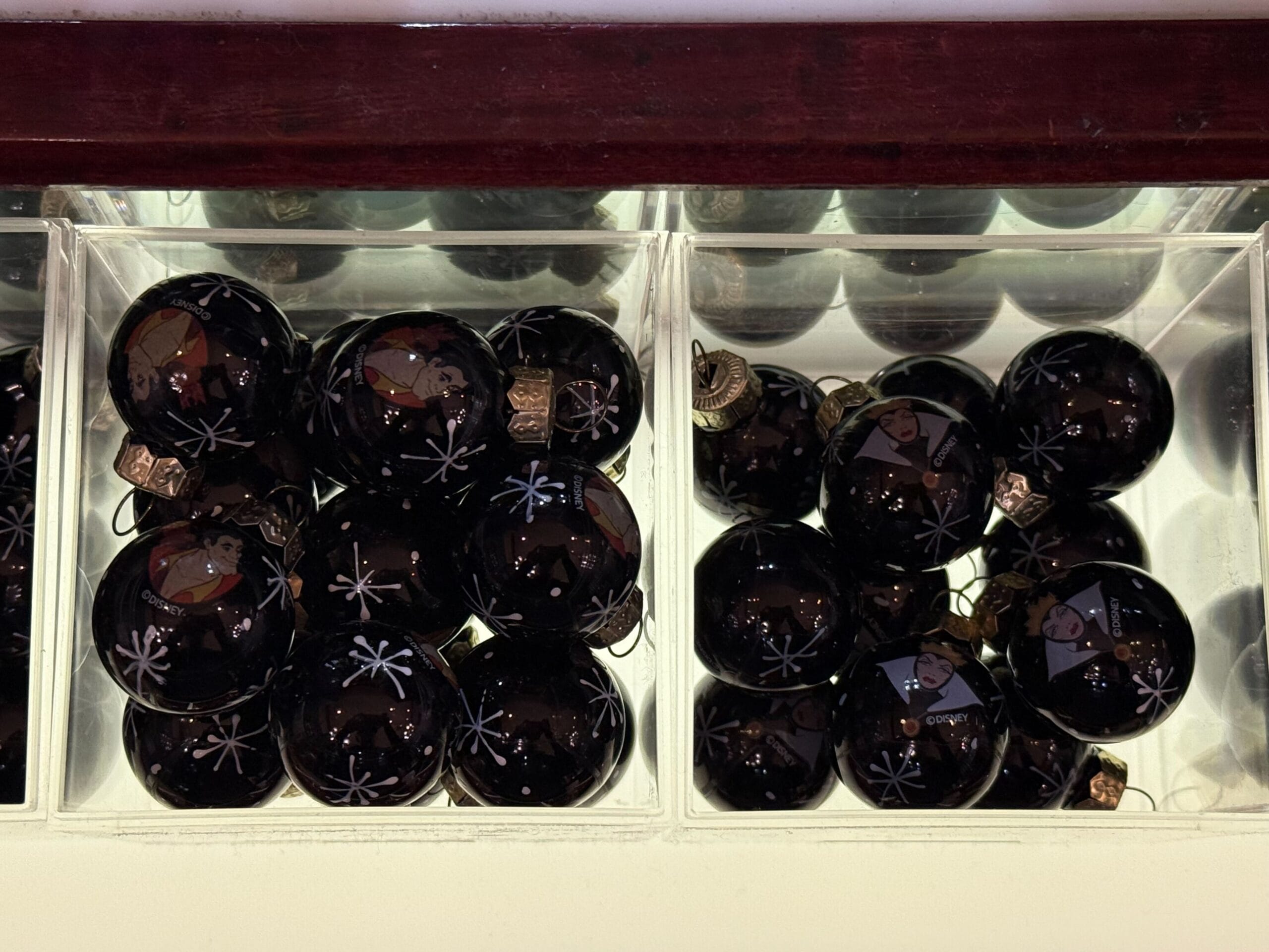 Black Christmas ornaments with white snowflake designs are displayed in clear divided containers.