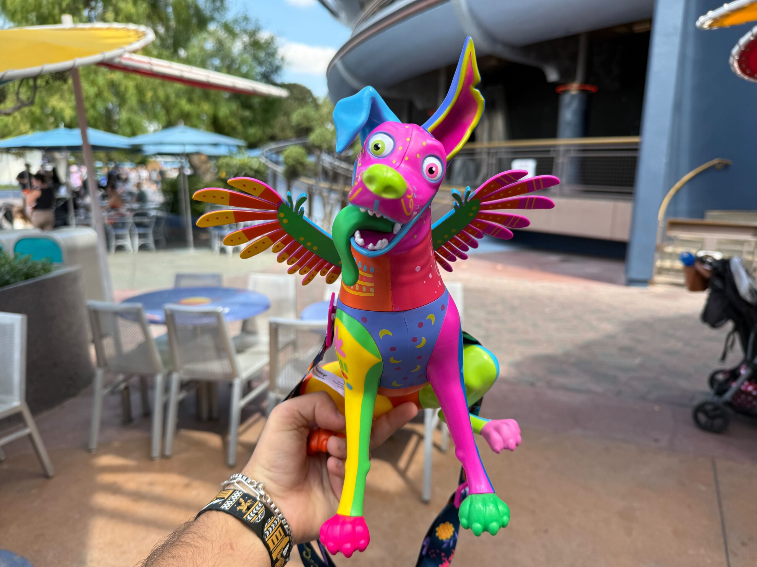 A colorful, winged dog figurine is held up outdoors at Plaza de la Familia, Disneyland Resort on a sunny day.