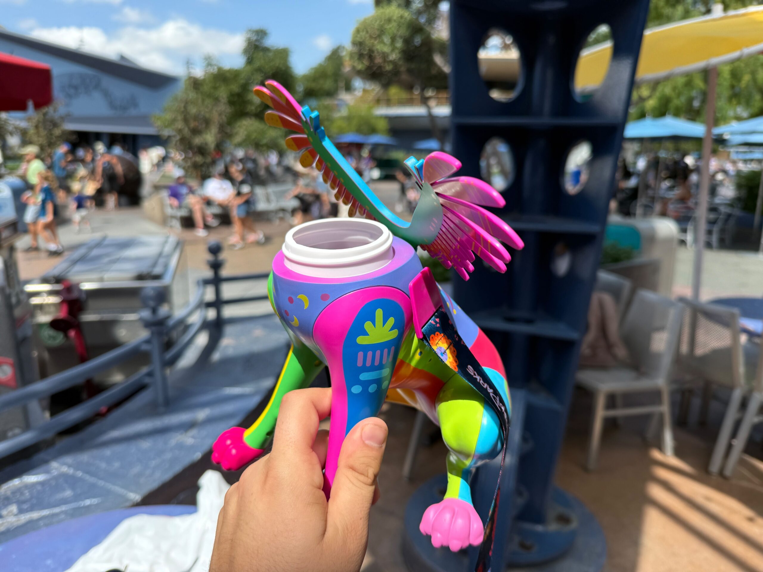 A hand holds a colorful Dante Sipper in an outdoor seating area at Disneyland Resort.