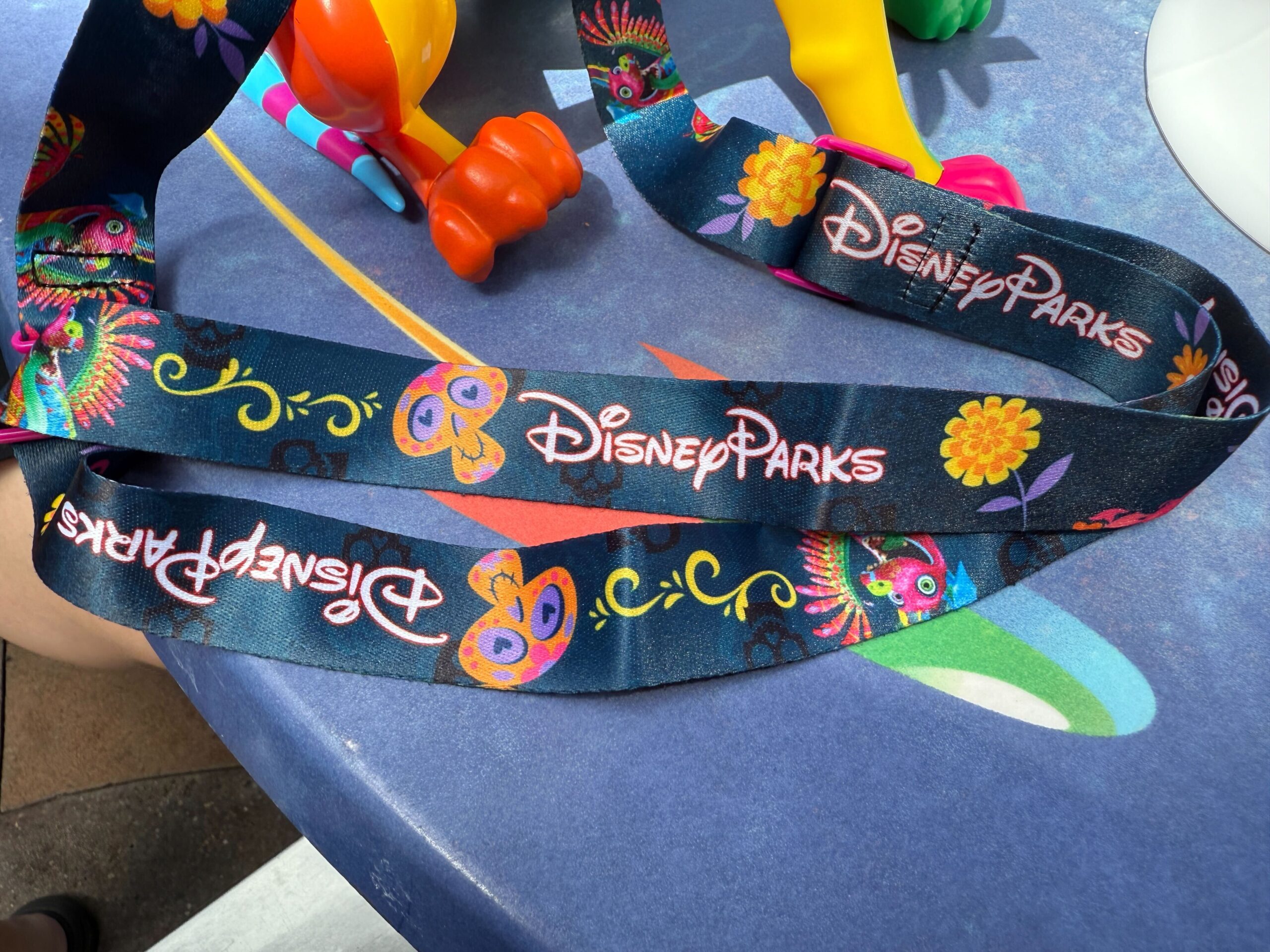 A Disney Parks lanyard with colorful floral designs lies on a blue table at Plaza de la Familia.