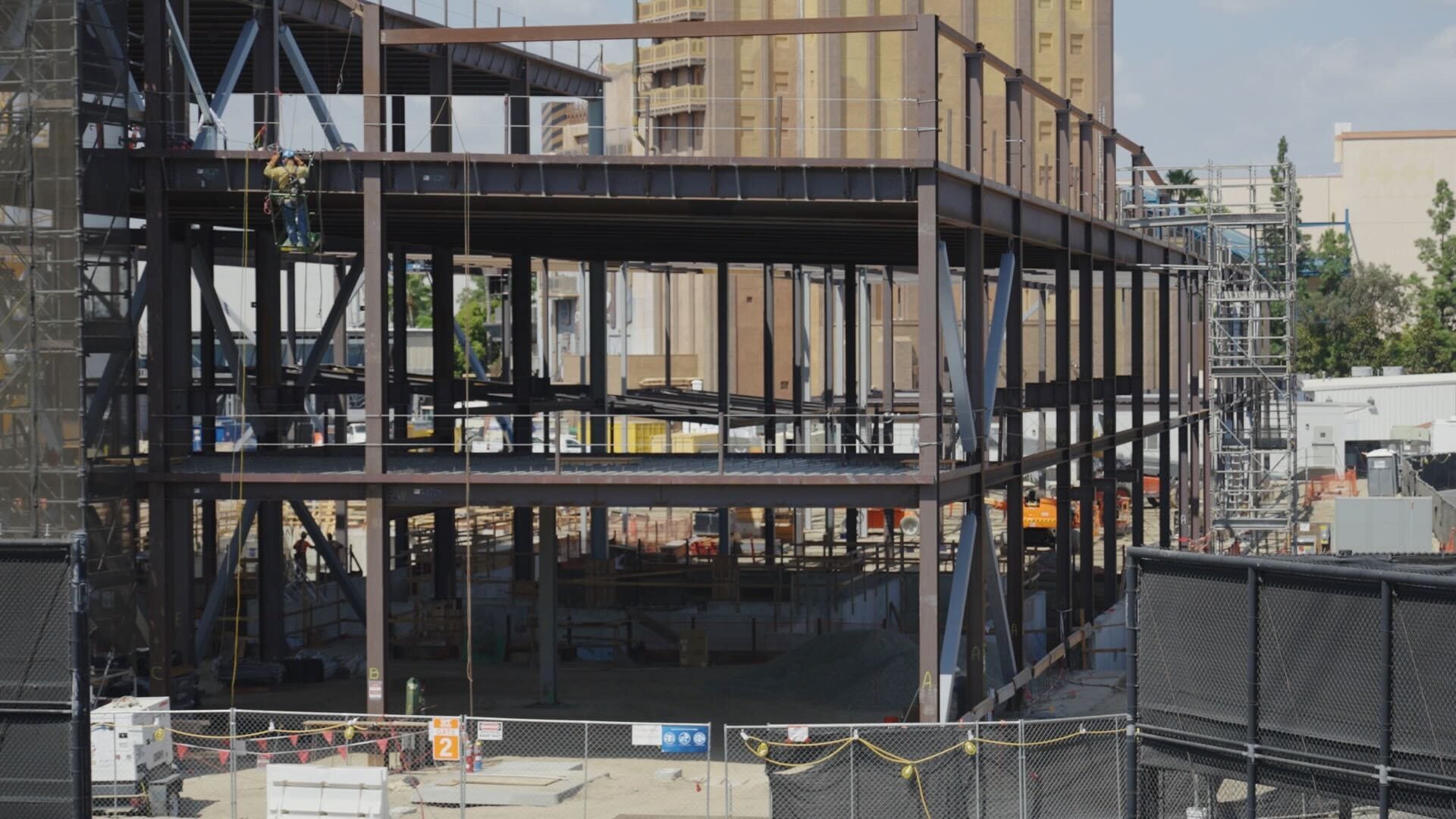Steel framework of a building under construction, with workers and equipment visible at the site.