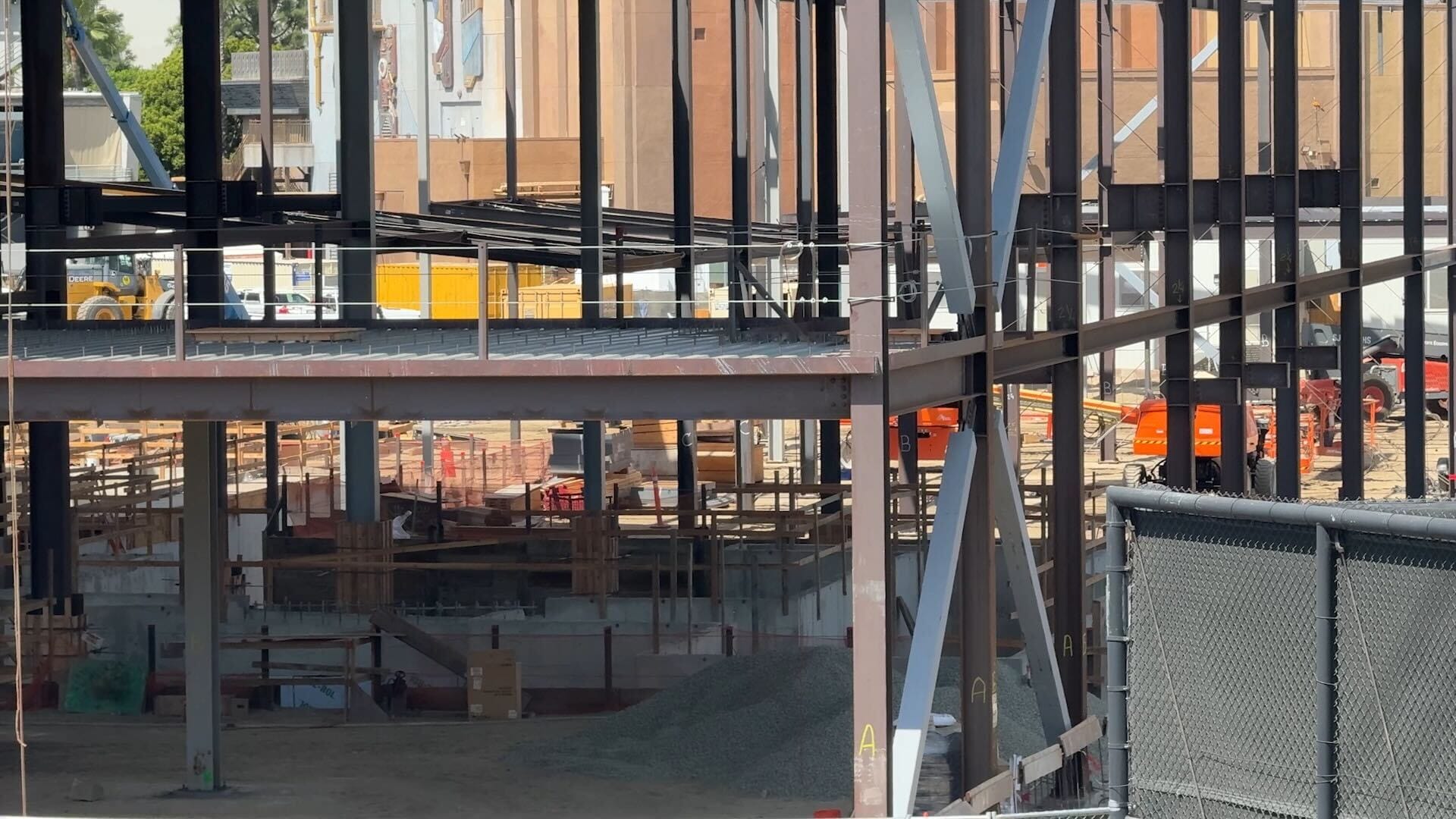 Steel framework of a building under construction, with equipment and materials scattered around the construction site.