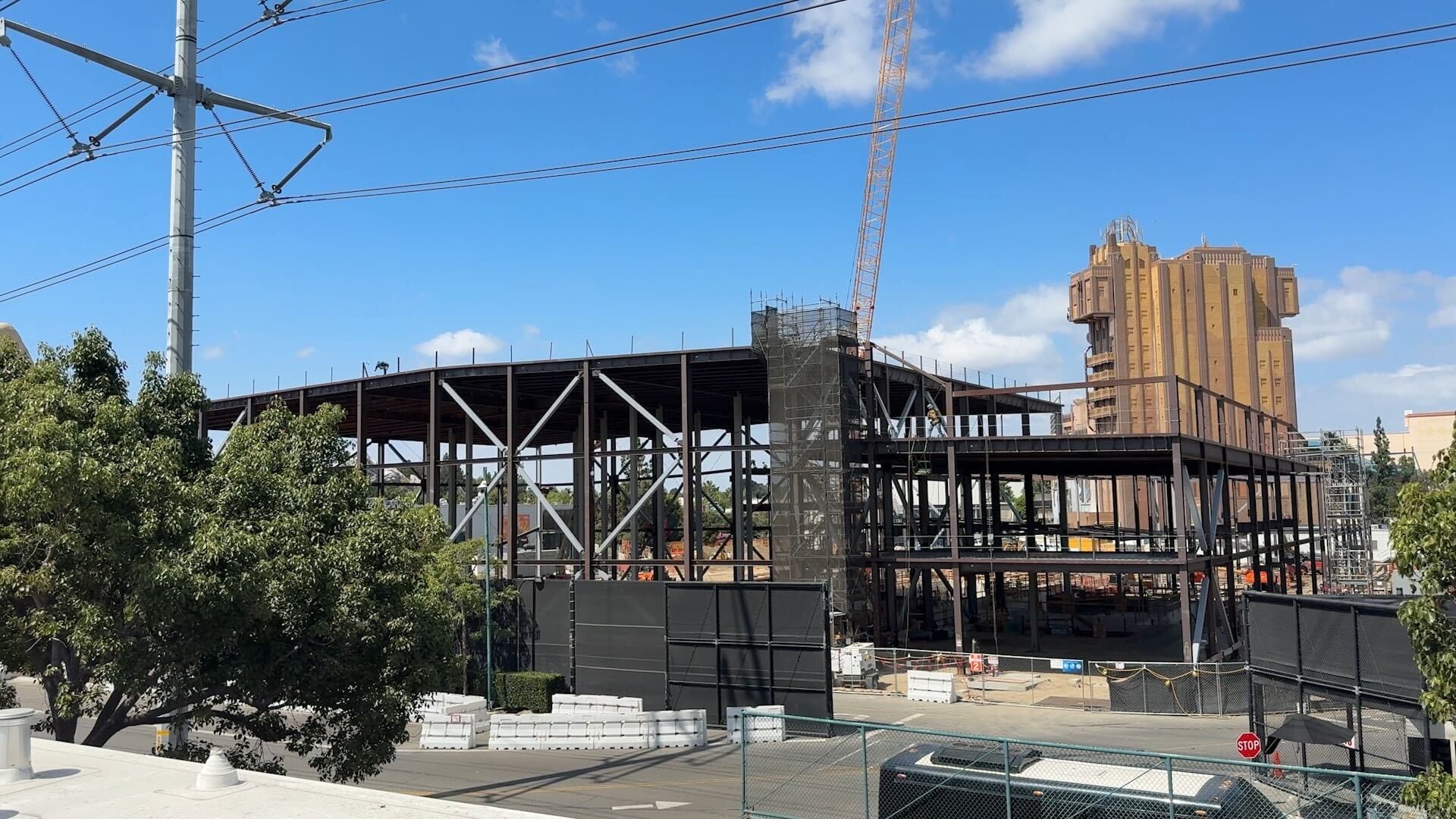 Steel framework of a building under construction with a crane and another tall structure in the background, under a blue sky.