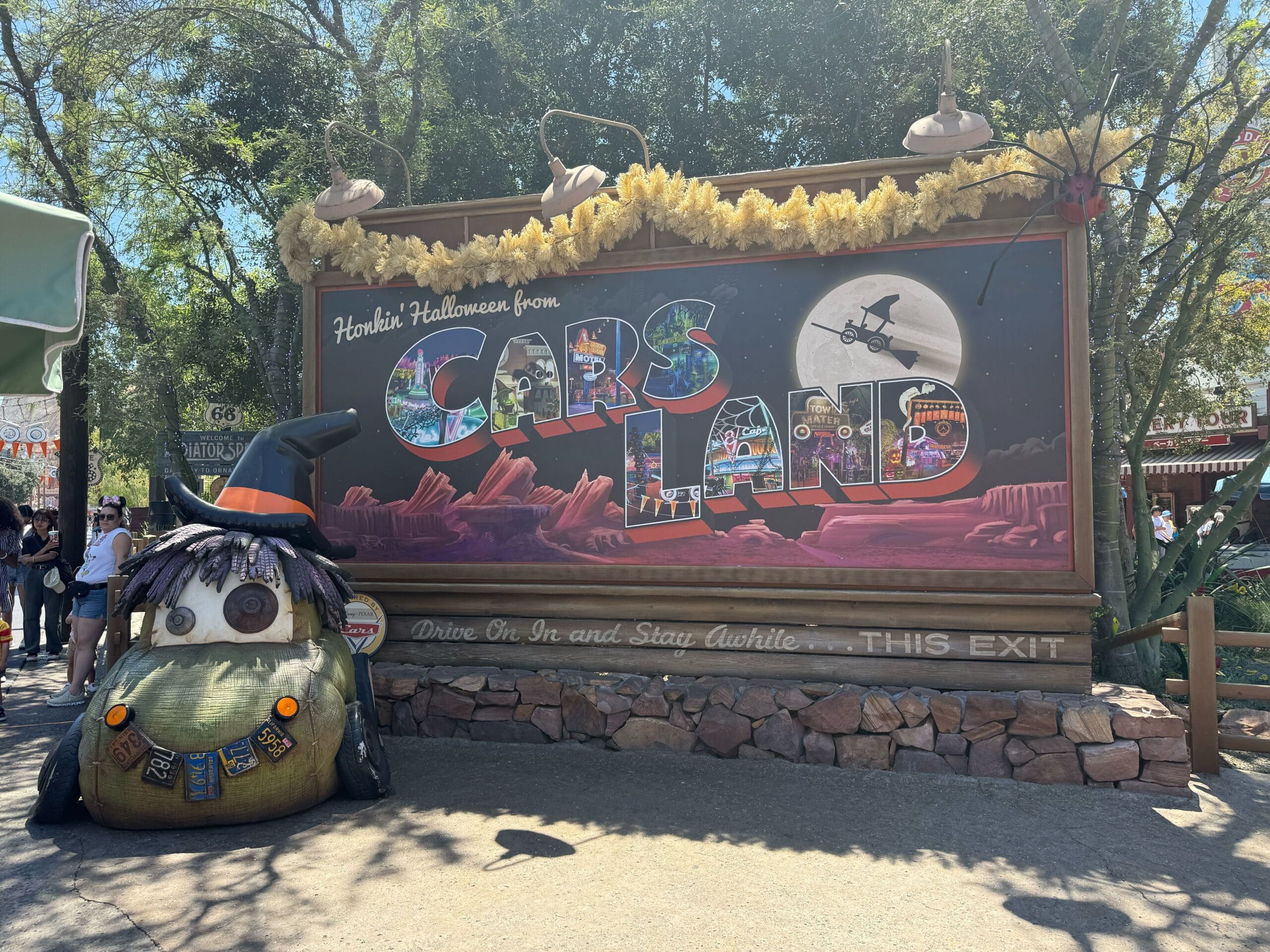 A Cars Land sign dressed for Halloween at Disneyland 2025, featuring a witch car statue and a spooky night sky illustration.