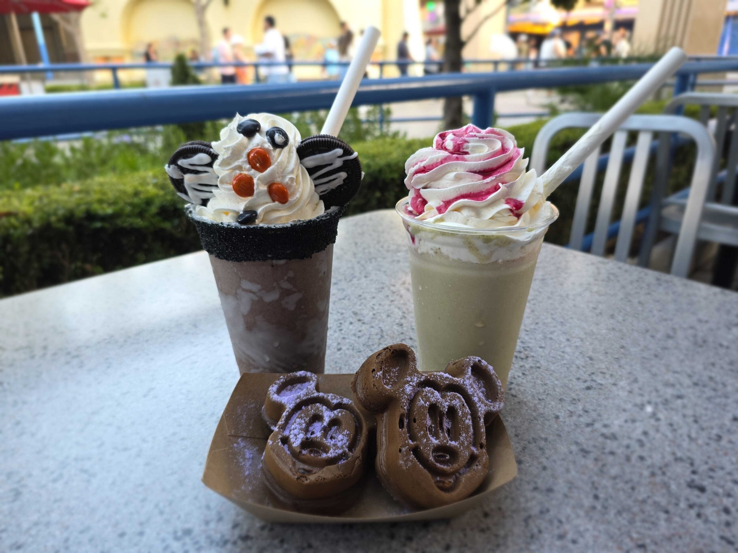 Two iced drinks and Mickey Mouse waffles are served outdoors at DL Halloween for a festive theme park treat.
