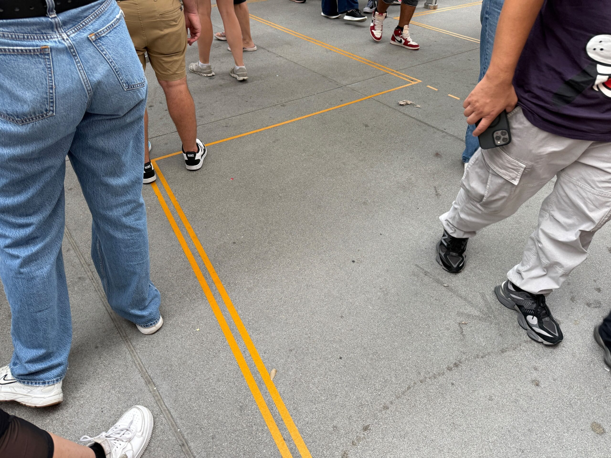 People standing on a sidewalk with yellow lines near Mickey & Minnie's Runaway Railway, holding phones and wearing casual clothes.