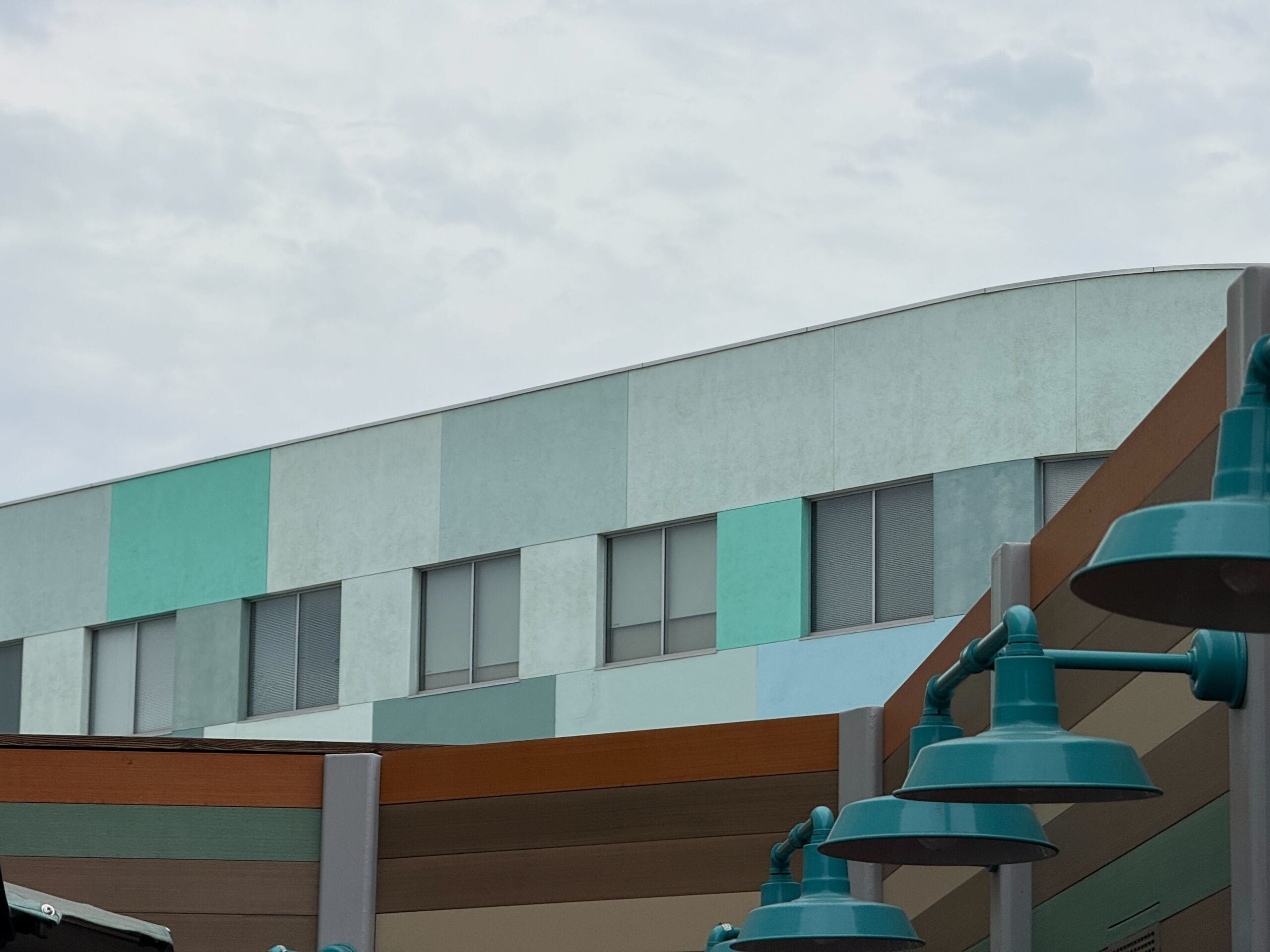 A building with pastel panels and teal lights, like Mickey & Minnie's Runaway Railway’s outdoor queue under a cloudy sky.