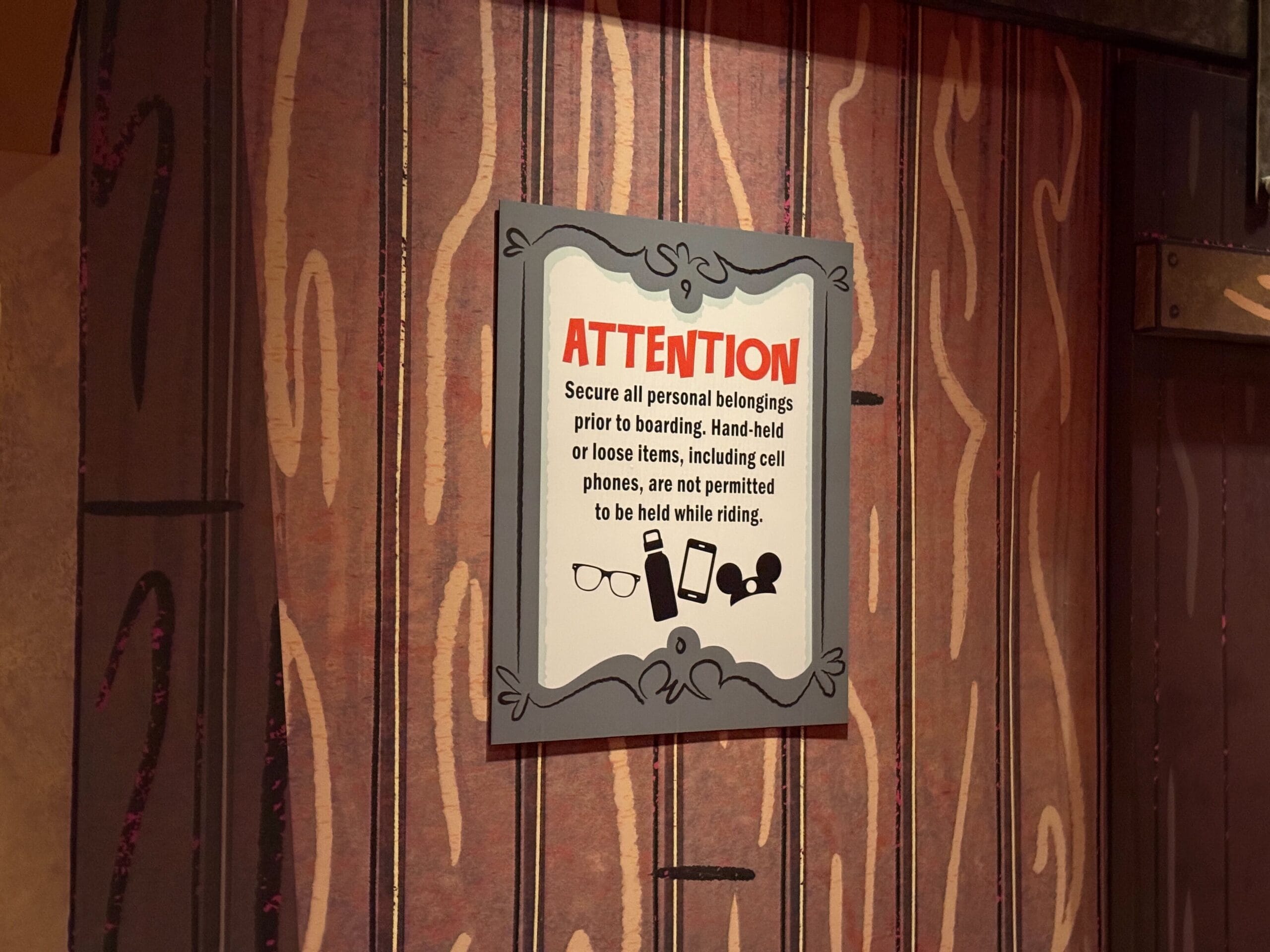 A sign in the outdoor queue for Mickey & Minnie's Runaway Railway warns riders to secure phones and glasses before boarding.