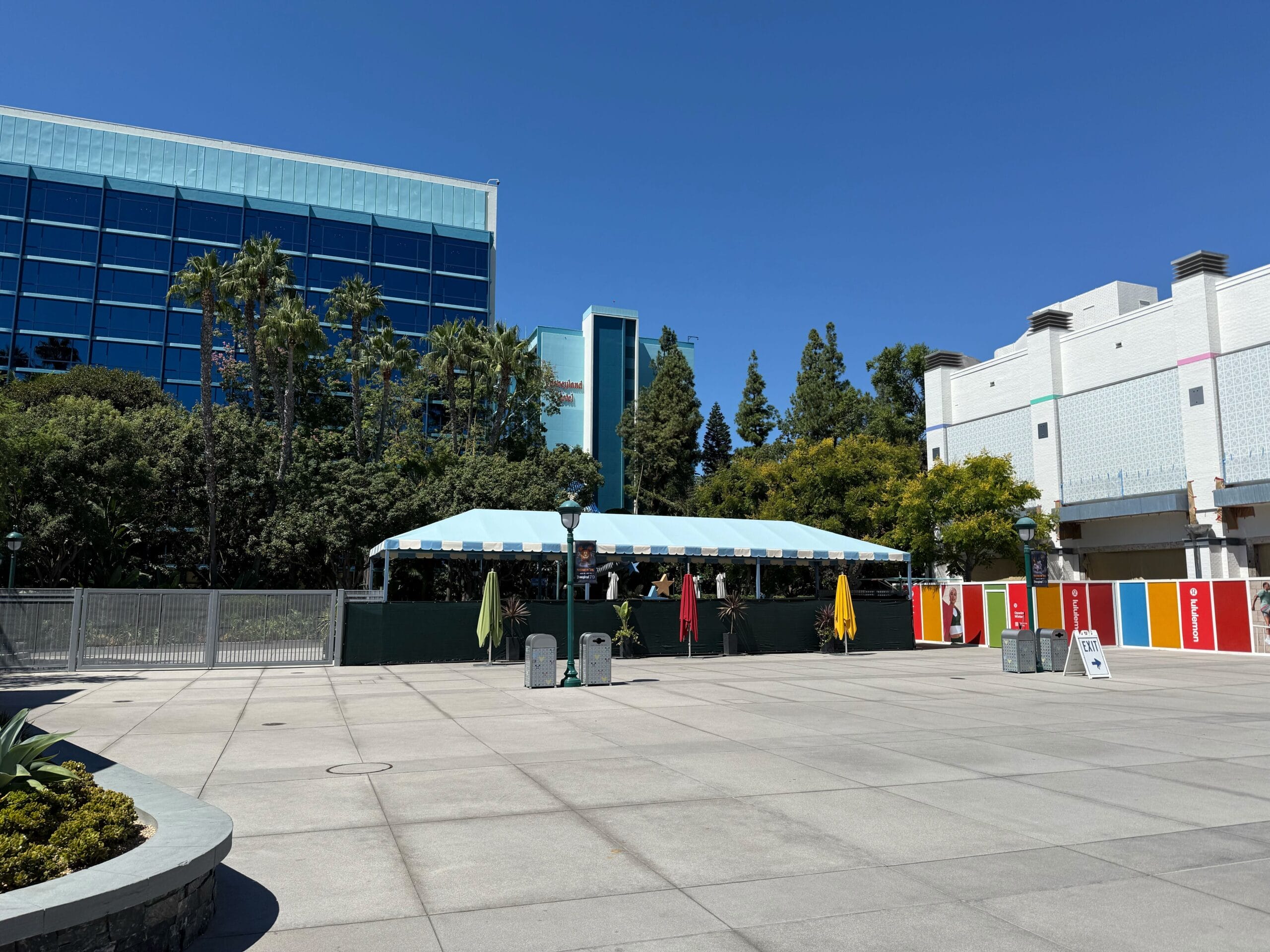 Outdoor seating area with a blue-and-white striped canopy near Downtown Disney District’s colorful construction walls.