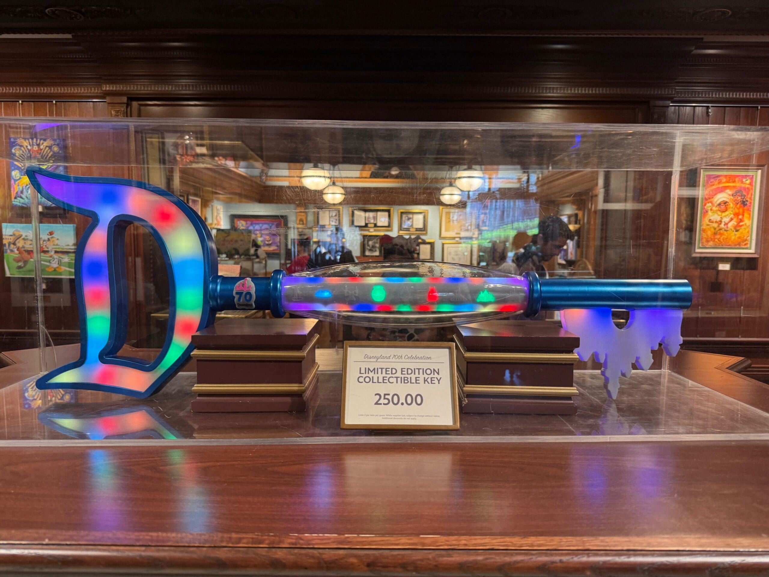 A Disneyland 70th Anniversary giant key with a “D” on one end, displayed in a glass case, priced at $250.