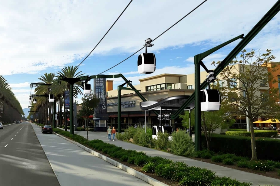 A street scene with a modern gondola system gliding above shops and palm trees near Disneyland under a blue sky.