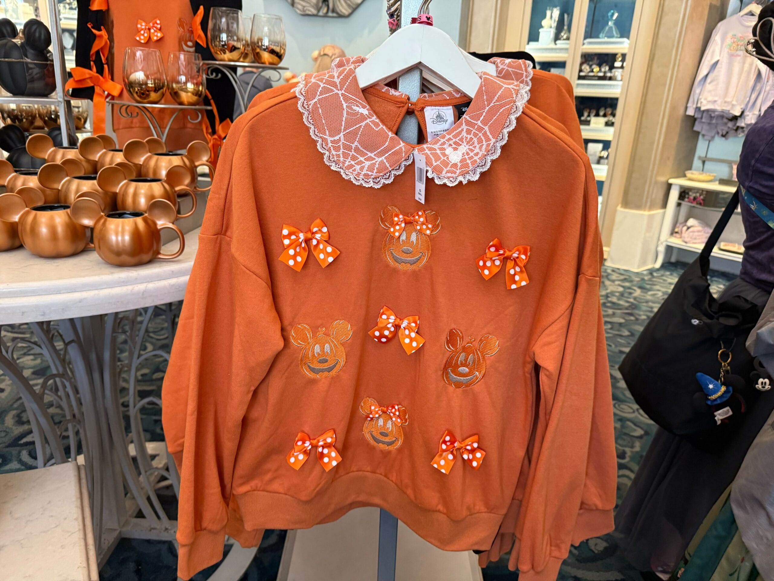 Orange sweatshirt with Minnie Mouse pumpkin faces and polka dot bows, part of 2025 Halloween Merchandise at Disneyland Resort.