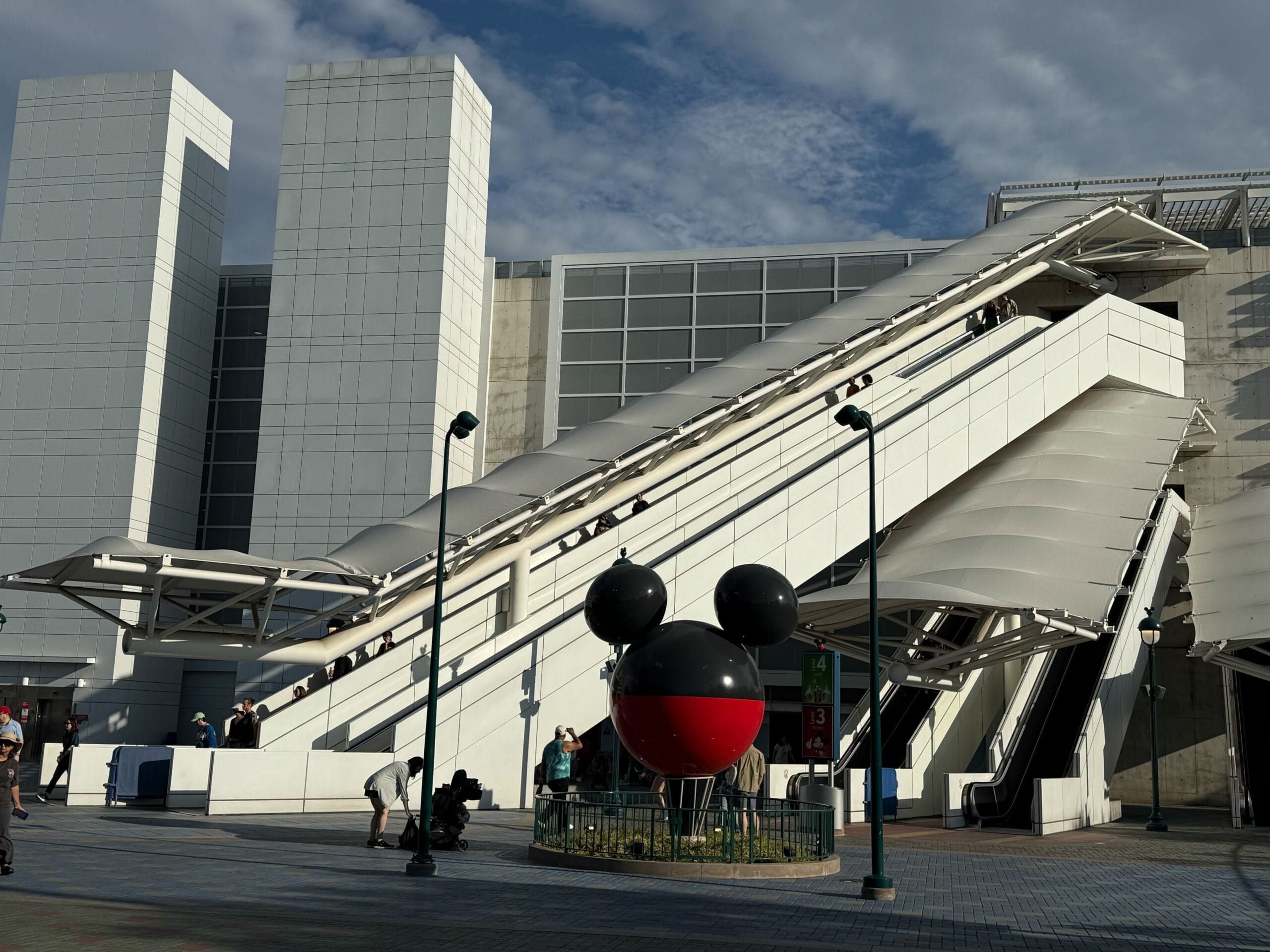 White modern building with large escalators; a black and red Mickey Mouse sculpture hints at Disneyland Resort magic.