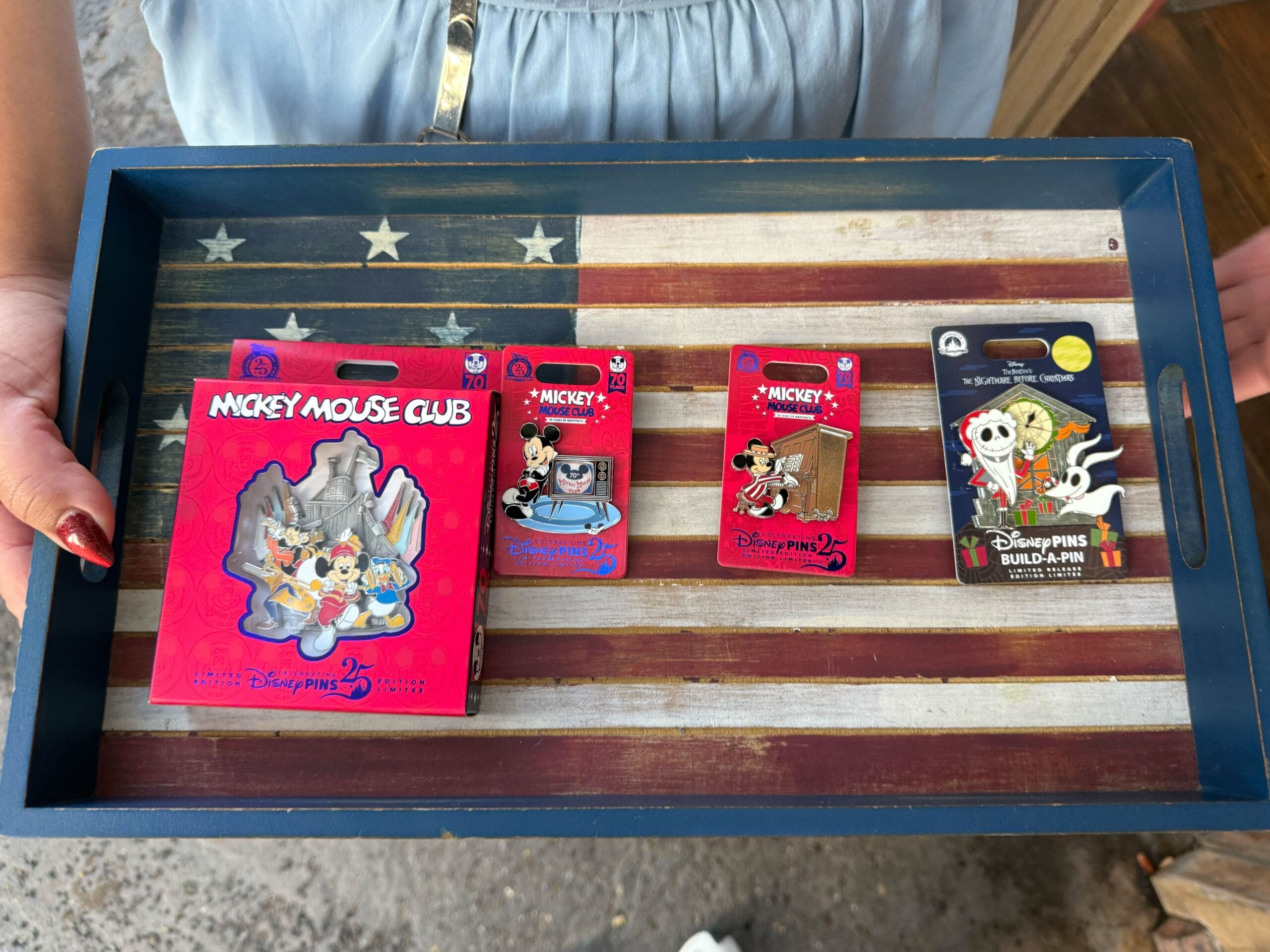 A person holds a tray with Disney pins displayed on an American flag background.