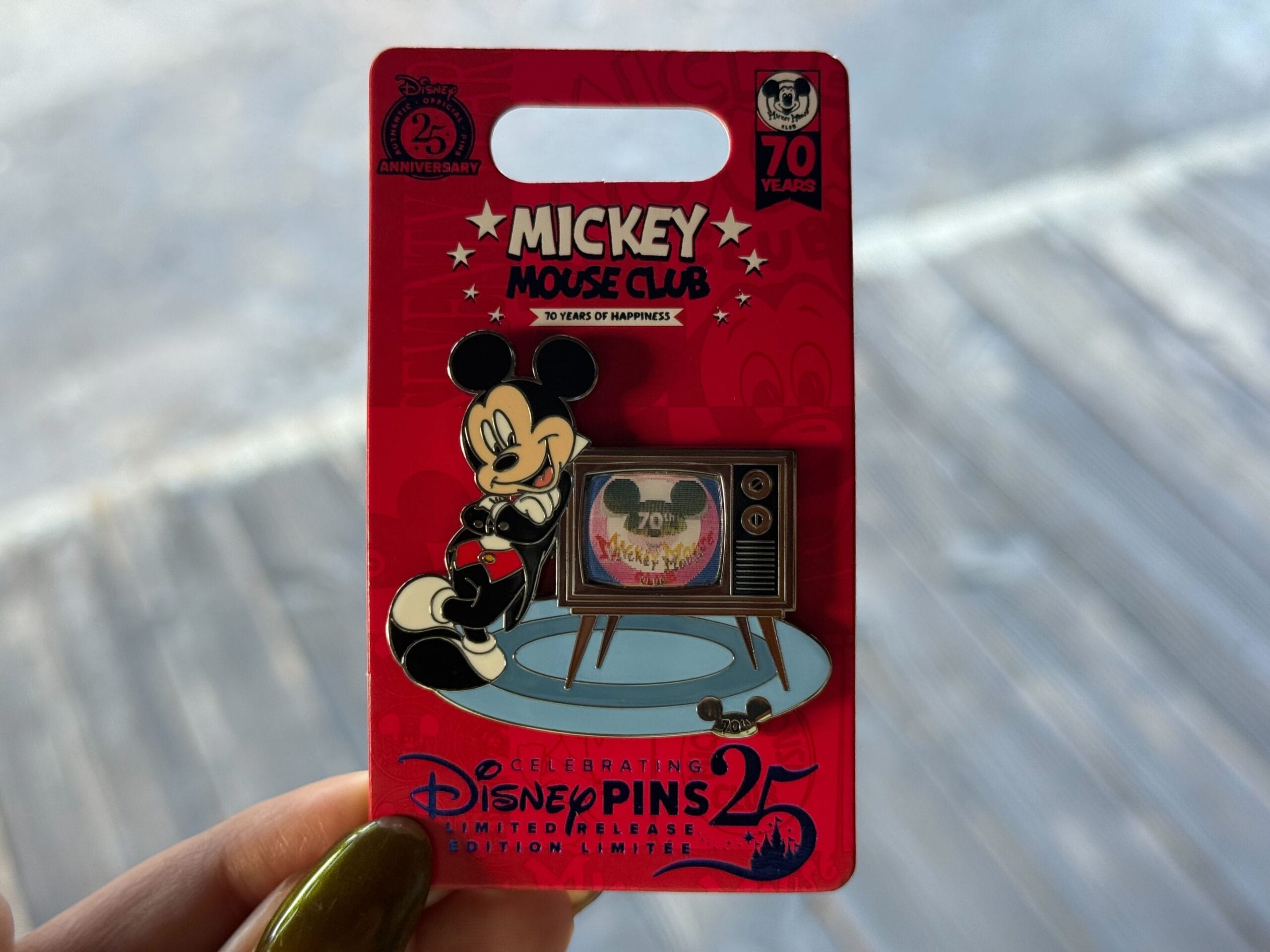 A hand holds a Mickey Mouse Club 70th anniversary limited edition Disney pin featuring Mickey and a retro TV.