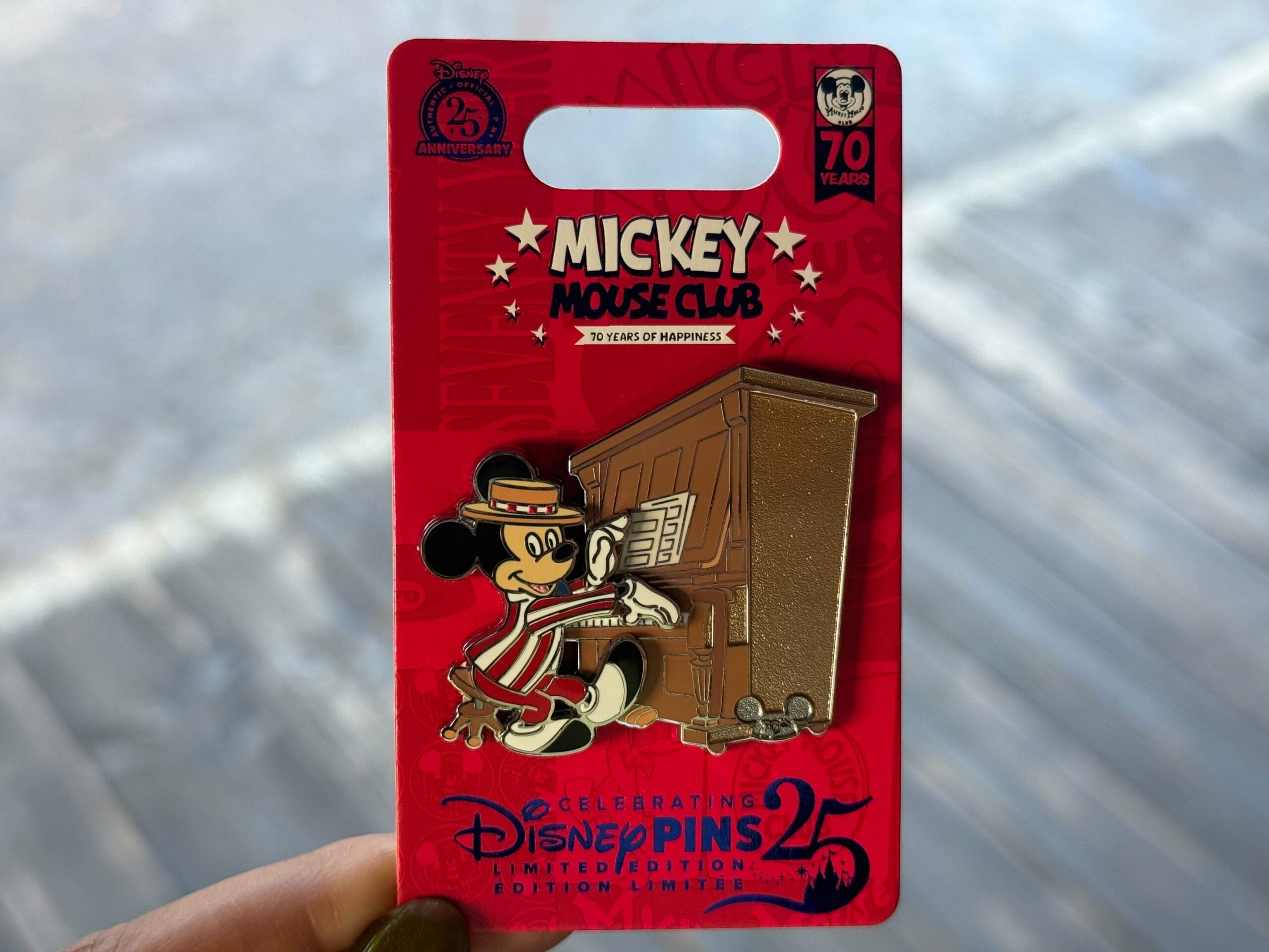 A Disney pin shows Mickey Mouse at a piano, celebrating DisneyPins 25 and Mickey Mouse Club’s 70th anniversary.