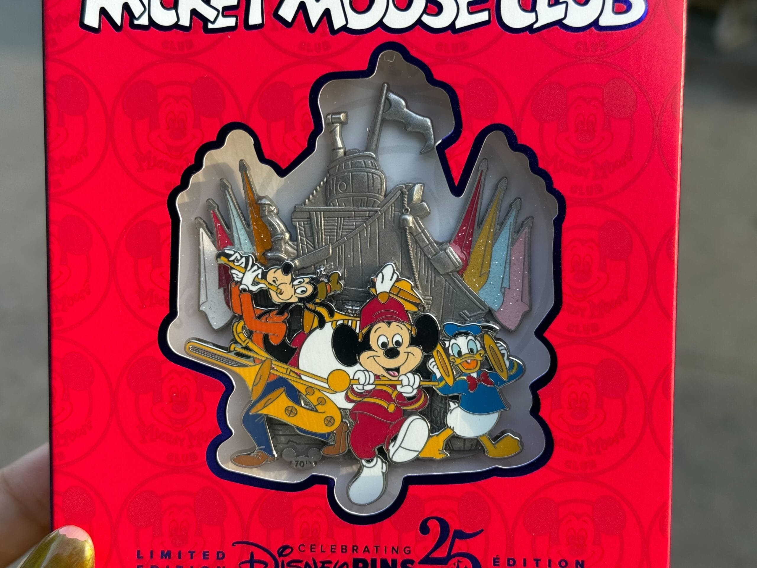 A Disney pin featuring Mickey, Goofy, and Donald in band uniforms with a ship in the background on red Mickey Mouse Club packaging.
