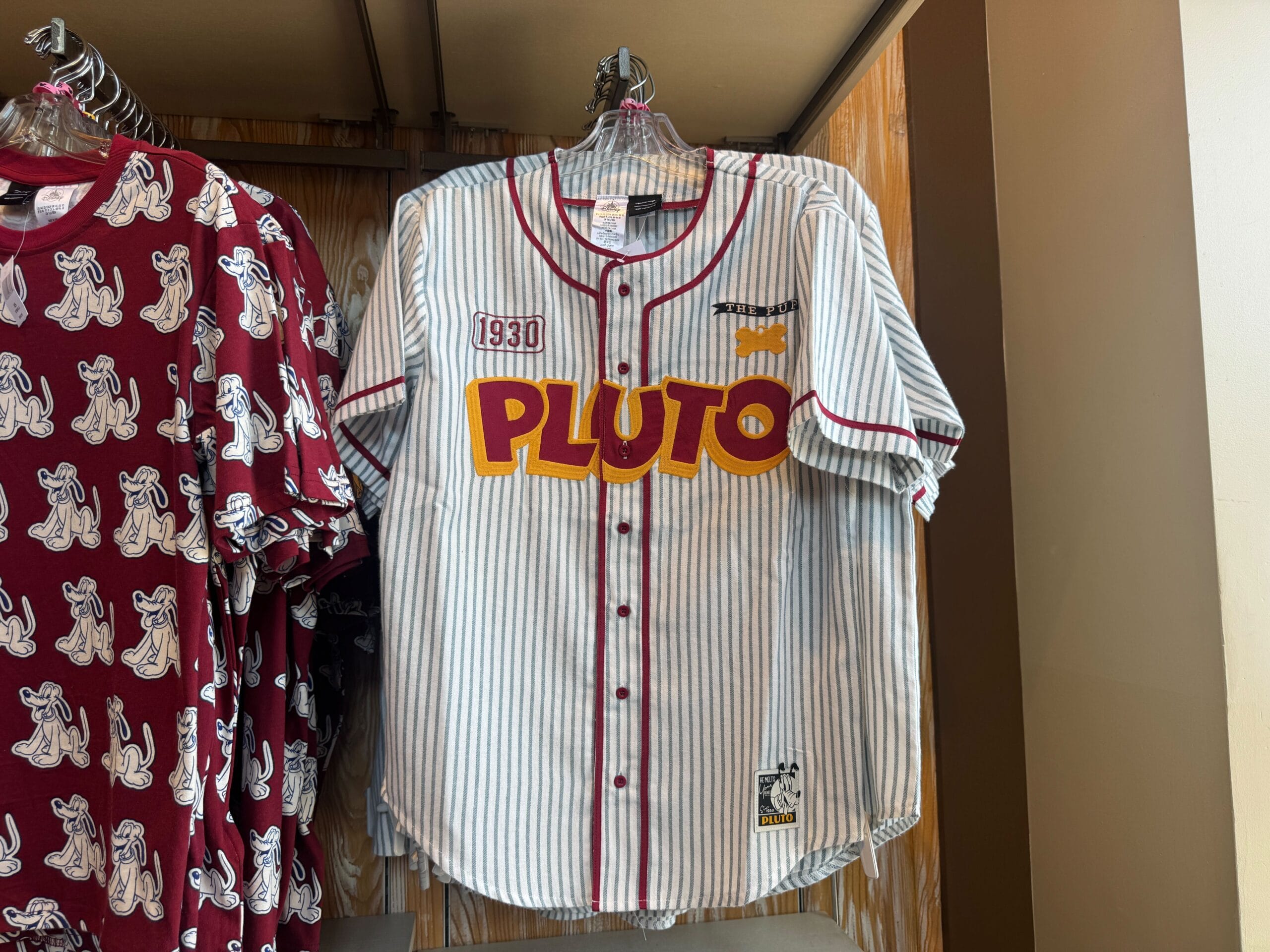 A white pinstriped baseball jersey with red trim, "PLUTO" and "1930" written on the front, hanging on a rack.
