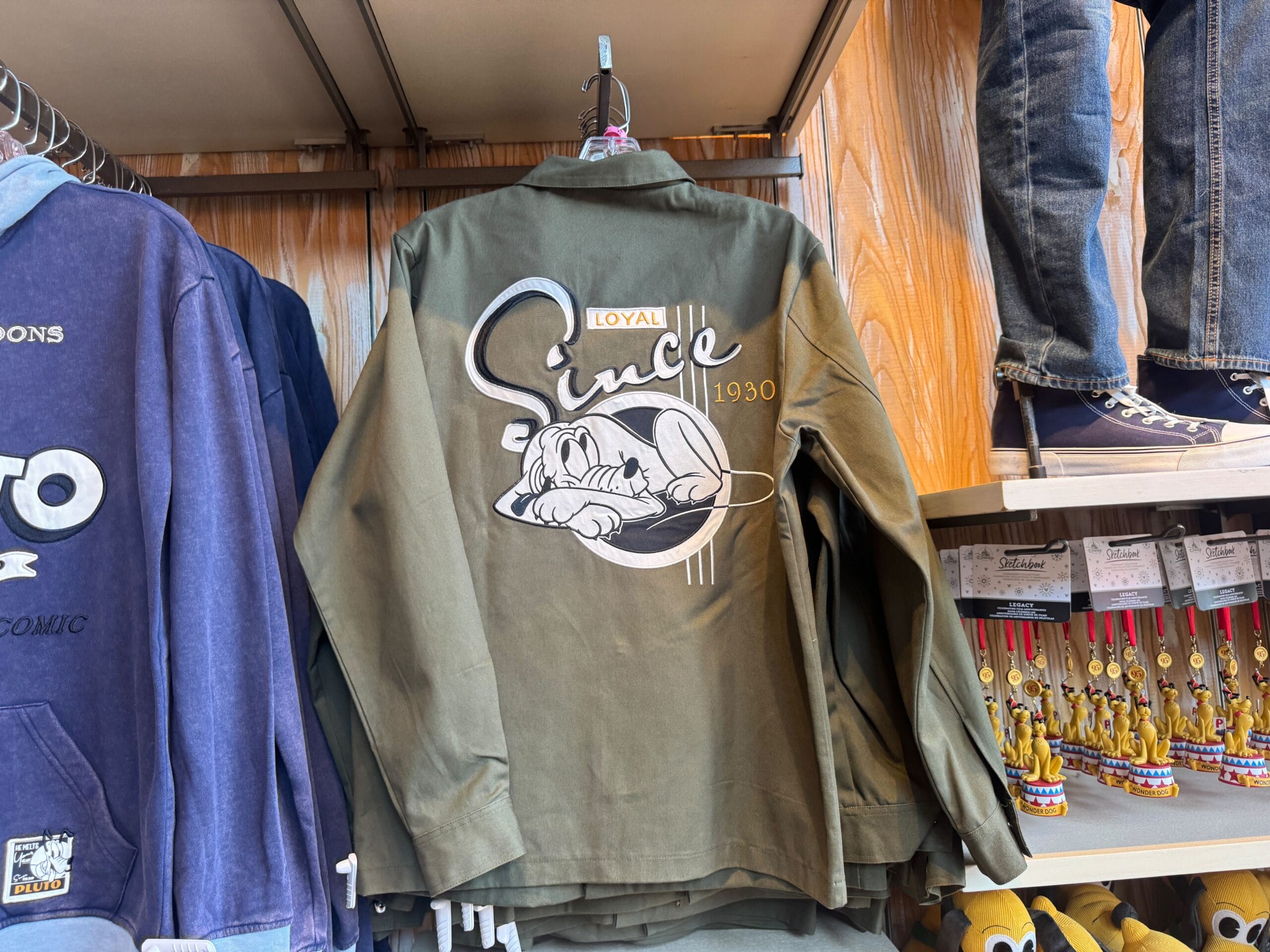 Olive green jacket with a sleeping dog and text reading "Loyal Since 1930" hanging on a store rack.