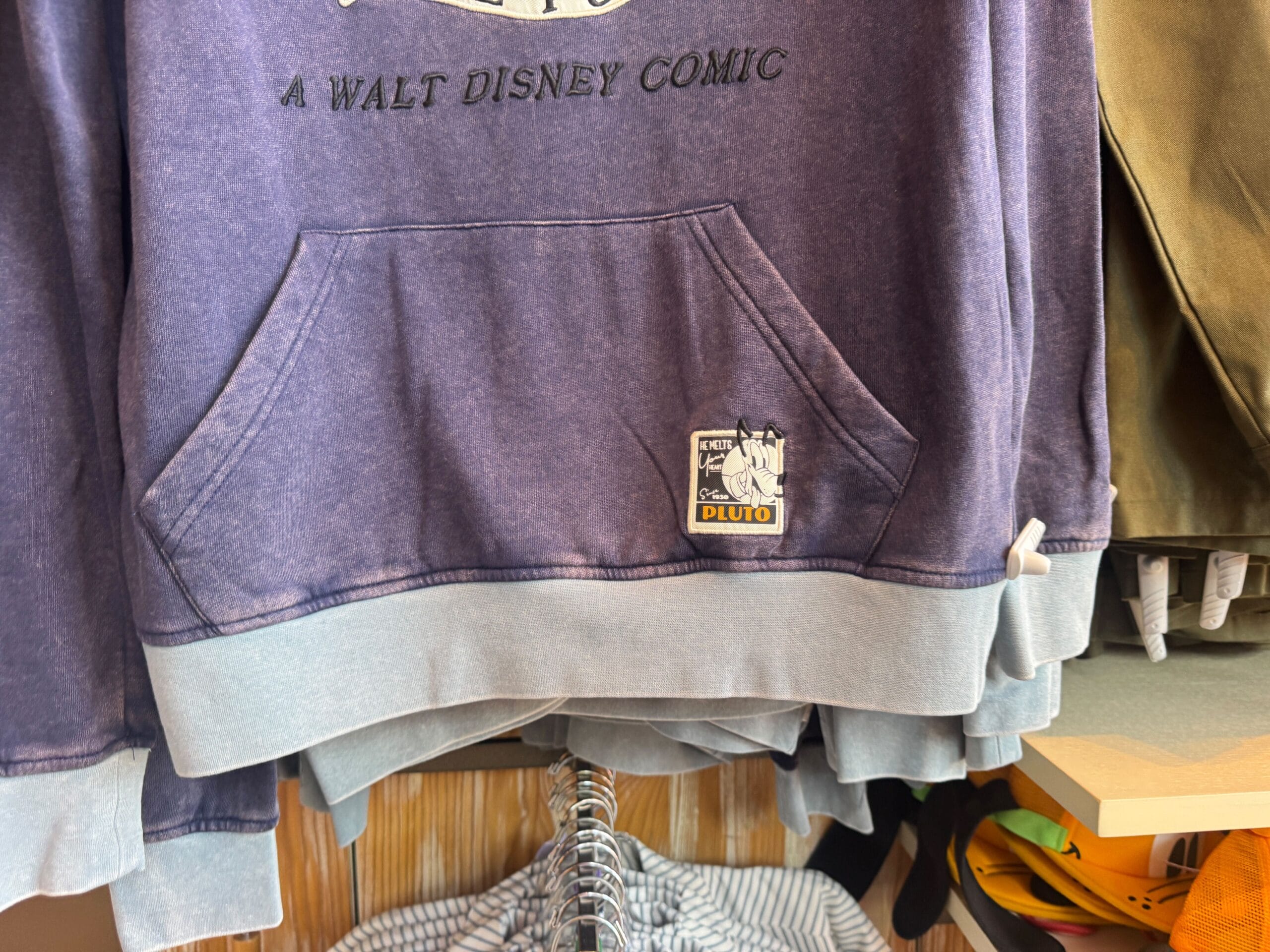 Purple Walt Disney Comic hoodie with a small Pluto cartoon patch near the front pocket, hanging on a clothing rack.