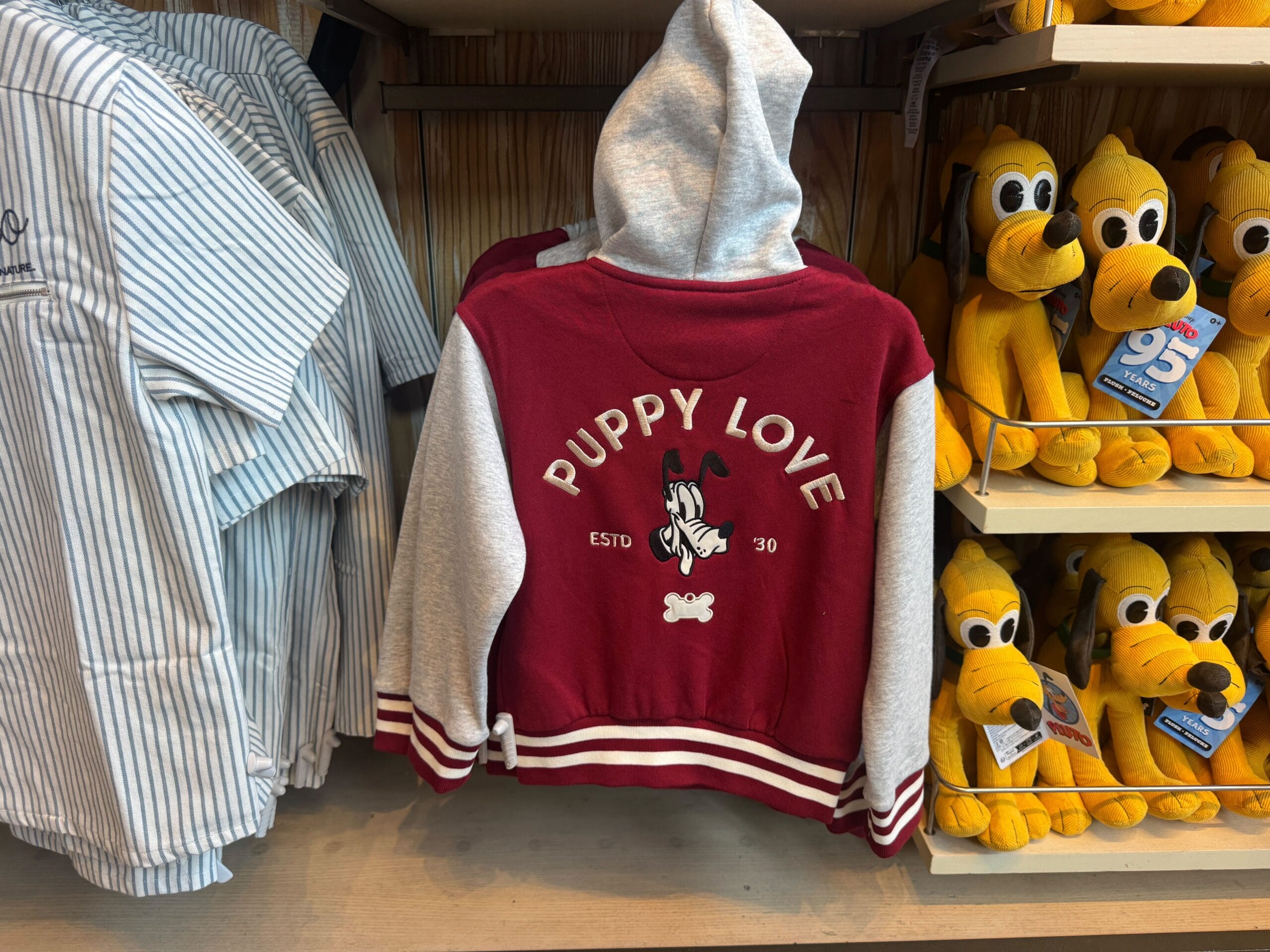 A red and gray hoodie with "Puppy Love" and a dog graphic, displayed next to yellow dog plush toys on a shelf.