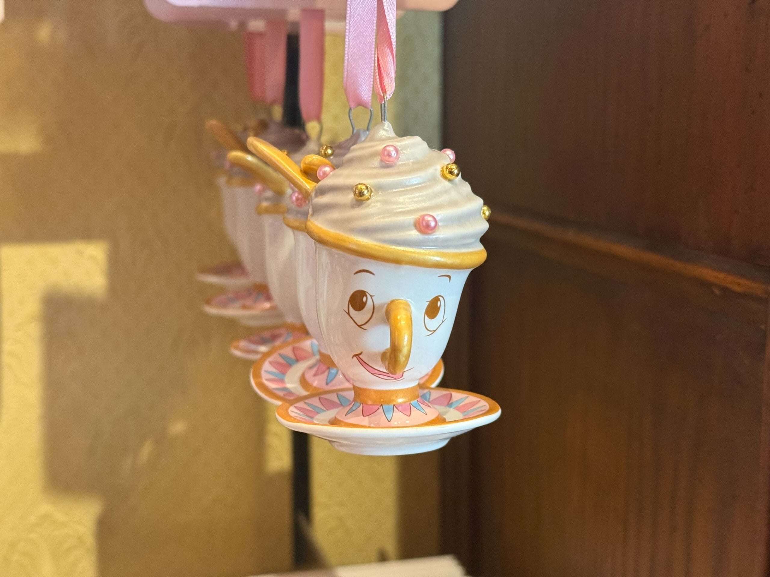 A smiling teacup ornament with gold handle, pink accents, and saucer; a charming addition to any Ornament Collection.