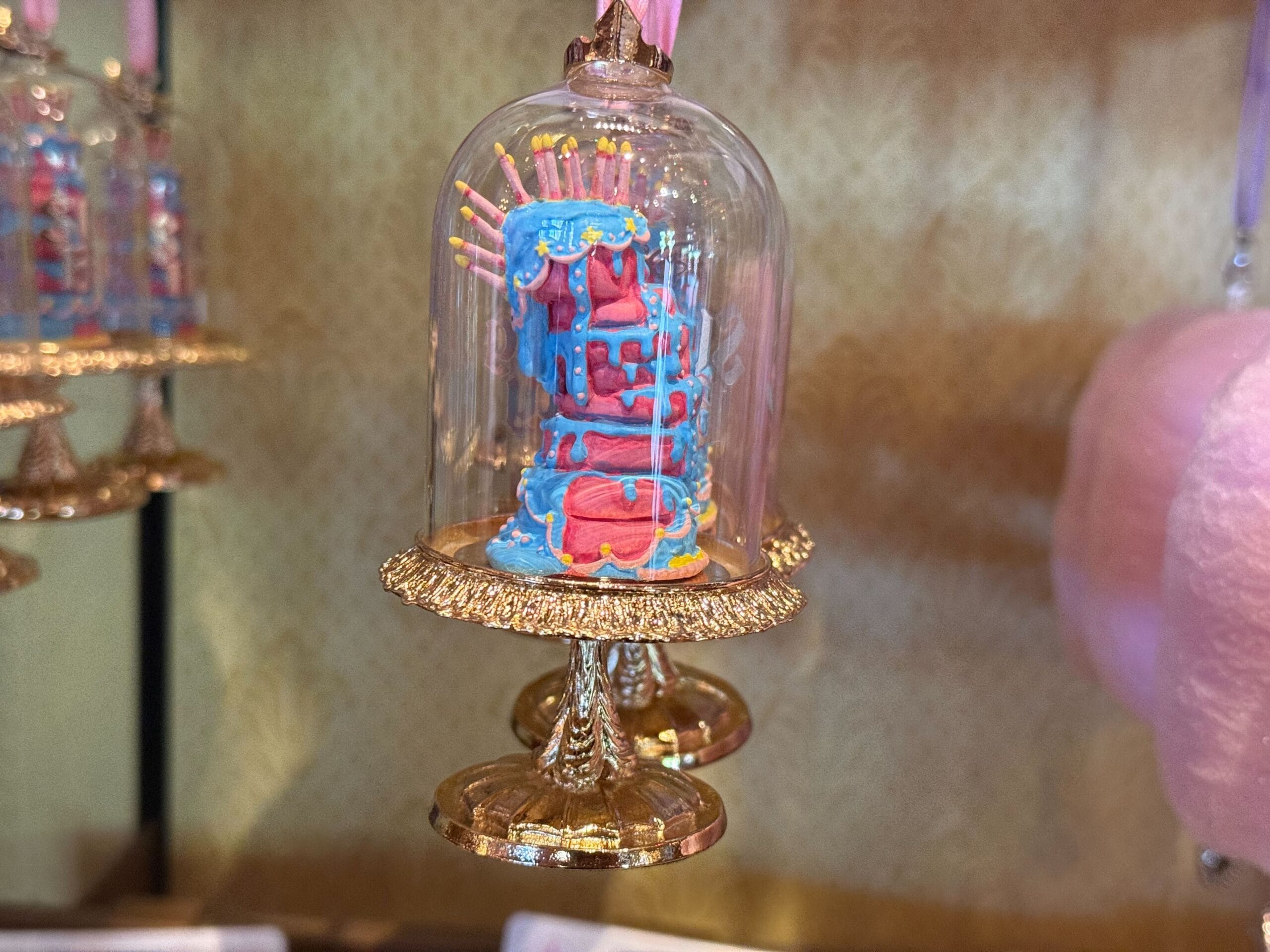 A mini blue and pink Sugarplum Princess Ornament under a glass dome with gold trim, displayed on a shelf.