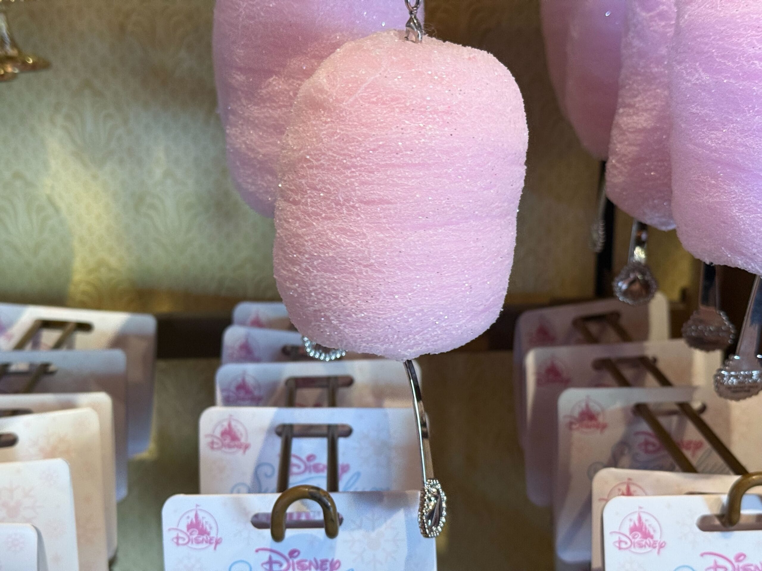 A pink Sugarplum Princess Ornament with glitter hangs in front of Disney-themed packaging on a display rack.