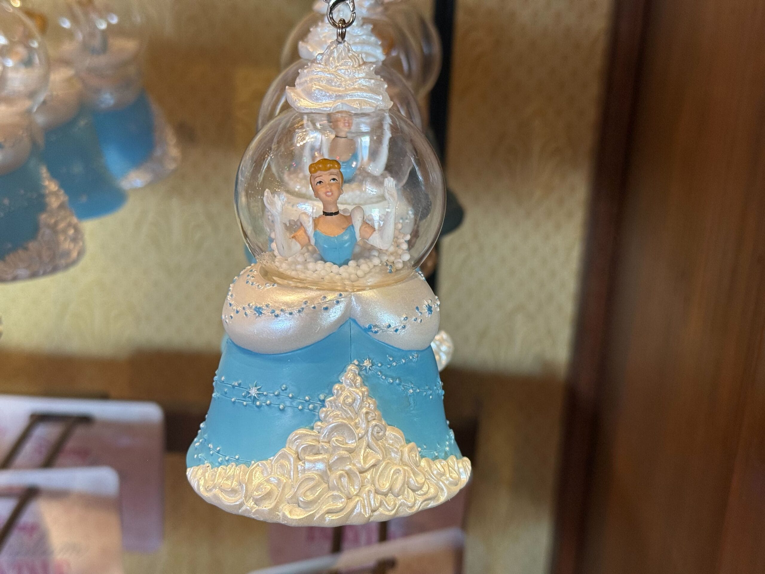 A Cinderella ornament from the Ornament Collection, in a blue and white dress, hangs on display in a clear globe.