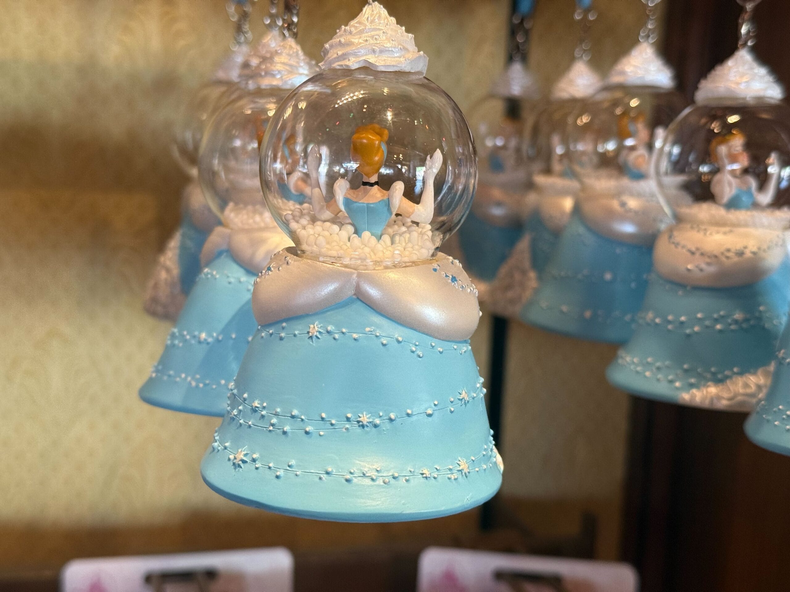 A Cinderella Sugarplum Princess Ornament shaped like a snow globe with a blue dress hangs on display.
