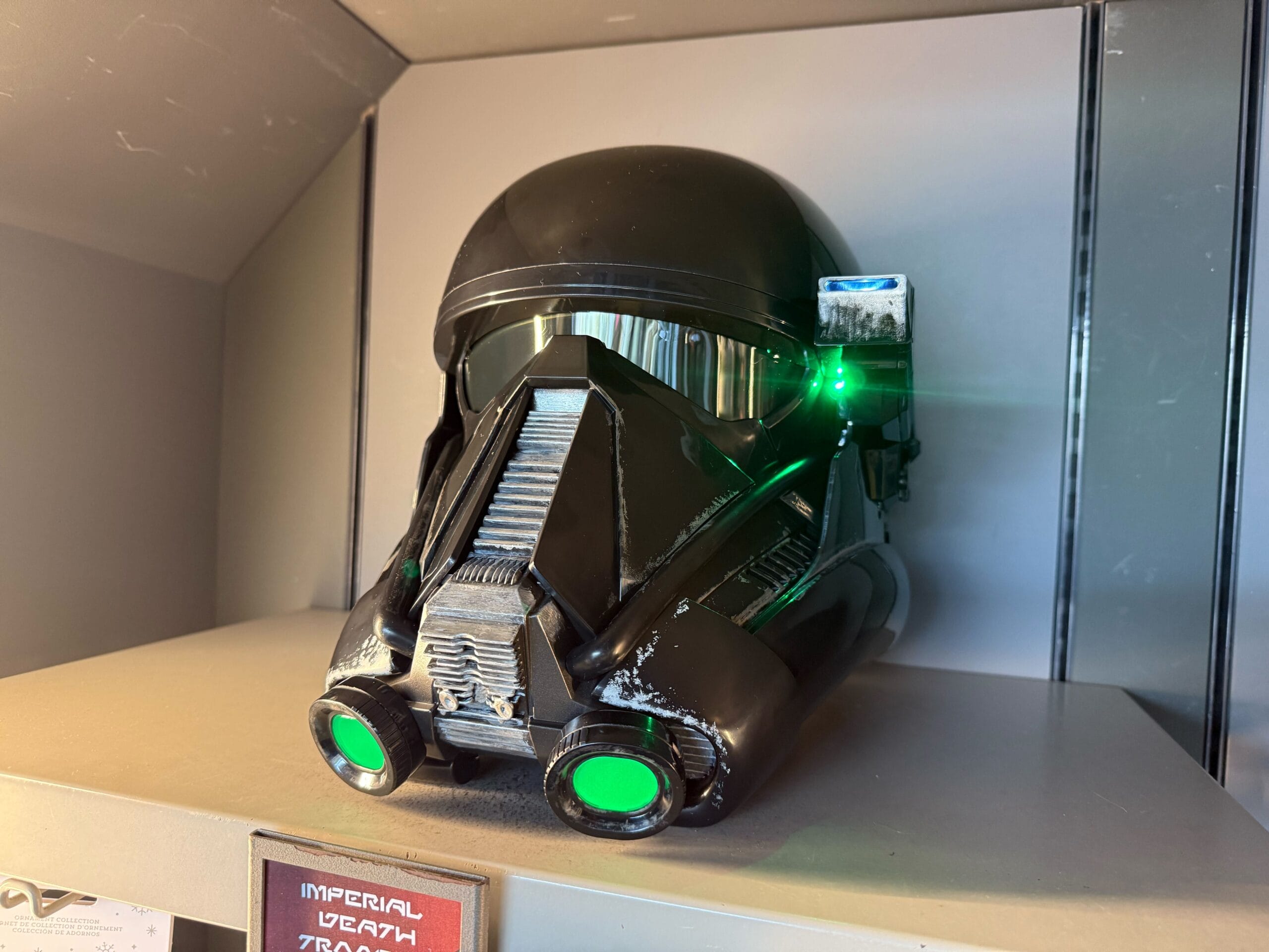 A black Star Wars Death Trooper helmet with green lights sits on a shelf at Star Wars Galaxy's Edge, Disneyland.