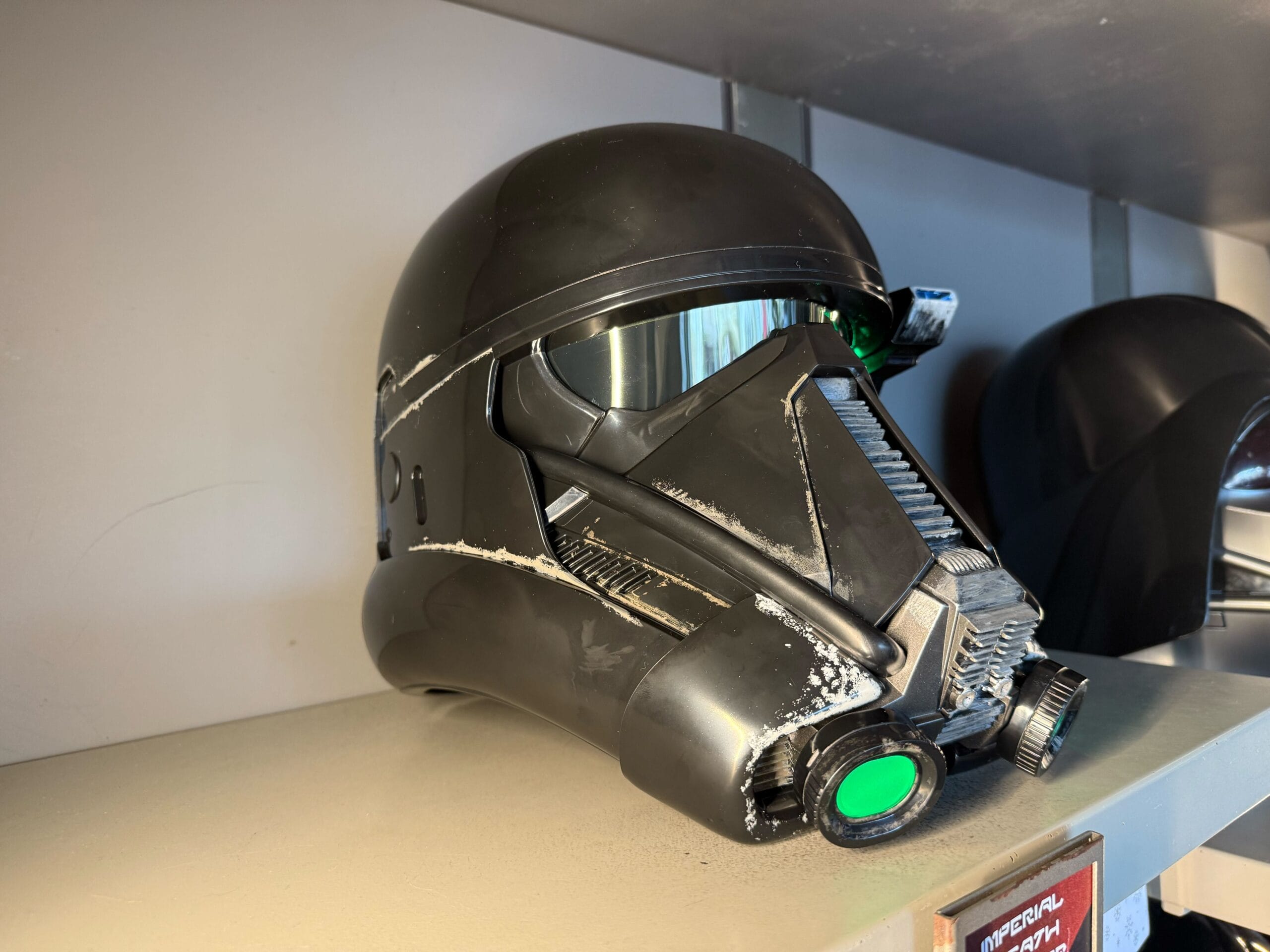 A black Star Wars Death Trooper helmet with green details sits on a beige shelf at Star Wars Galaxy's Edge.