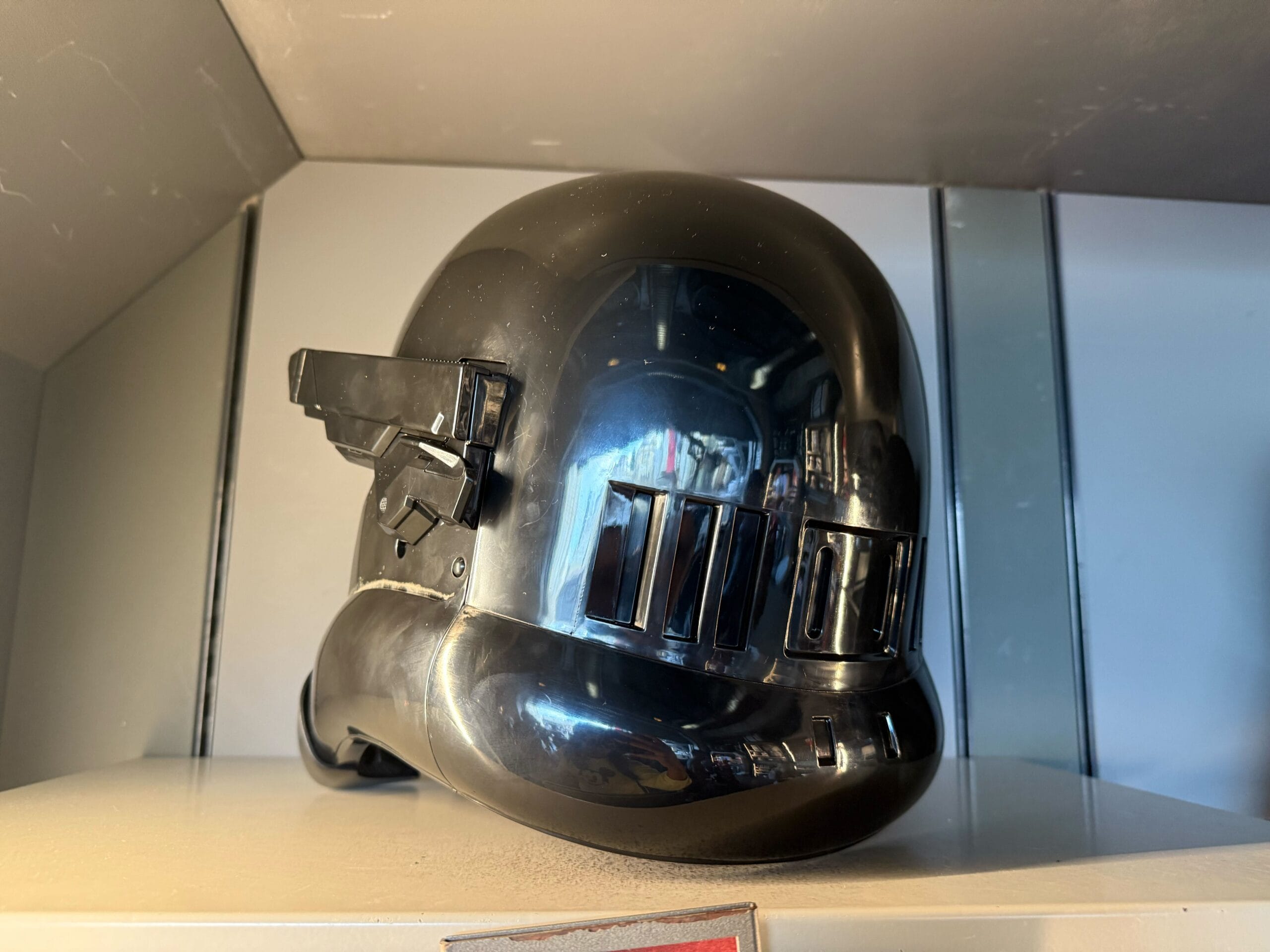 A glossy black Star Wars helmet with a futuristic design displayed on a shelf under bright lighting.