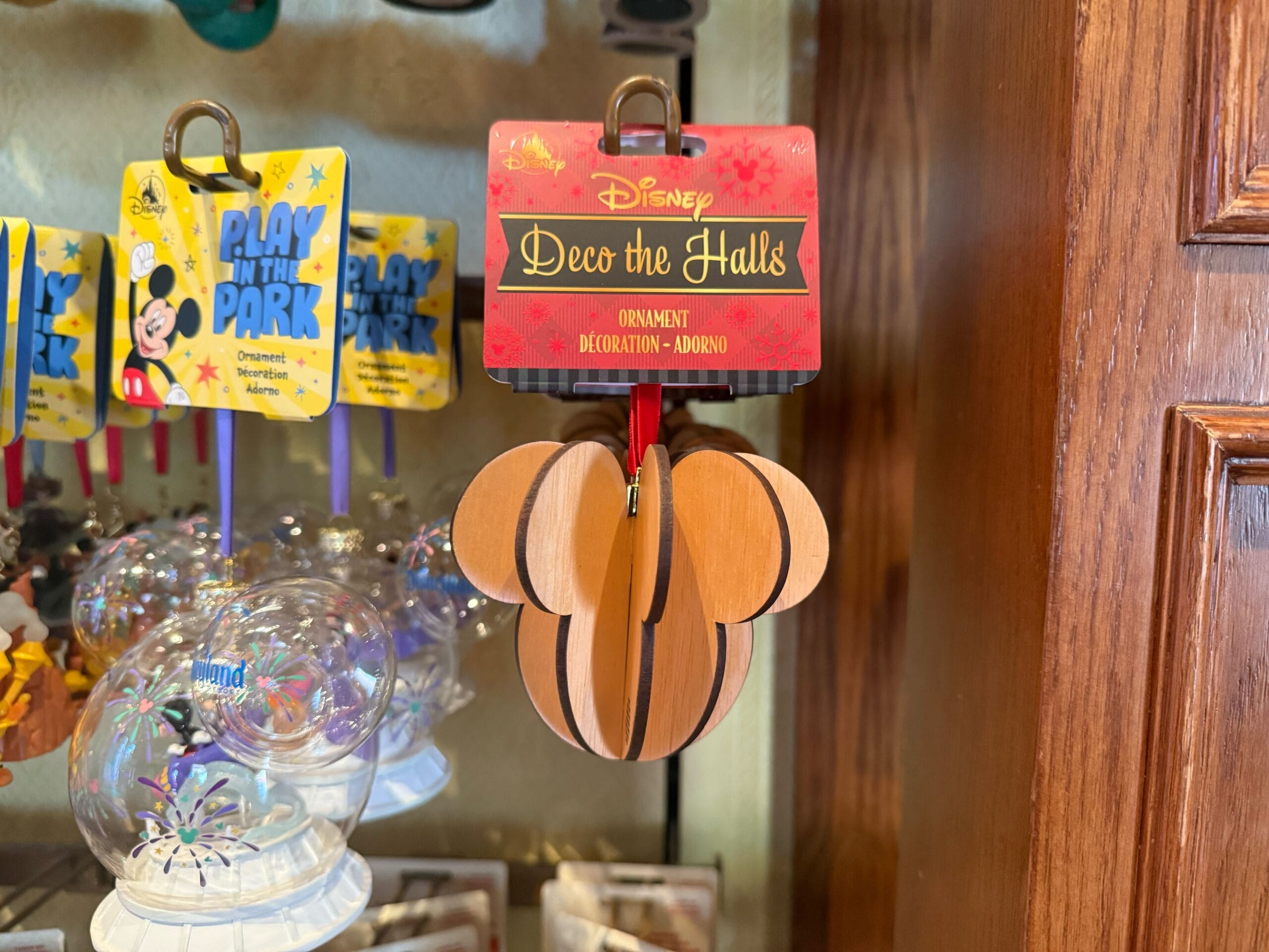 A wooden Mickey Mouse head ornament labeled "Deco the Halls" hangs on display among other Disney Christmas decorations.