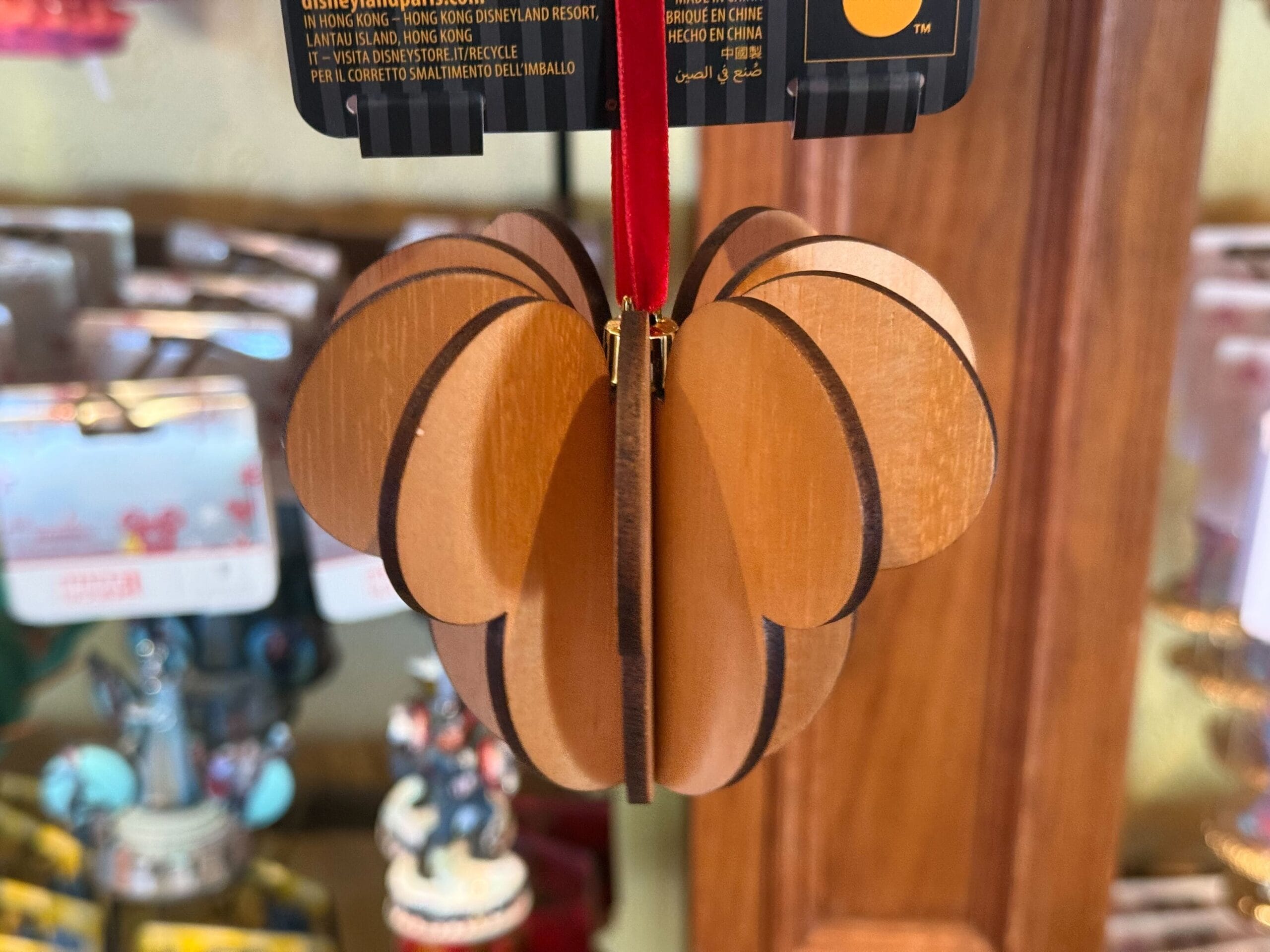 A wooden ornament shaped like a pumpkin hangs on display in a store with other decorations in the background.