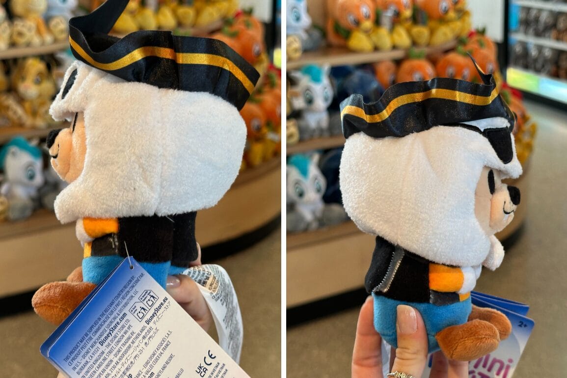 A person holds a plush toy of Mickey Mouse dressed as a pirate in a store with Goofy plush toys on the shelves.