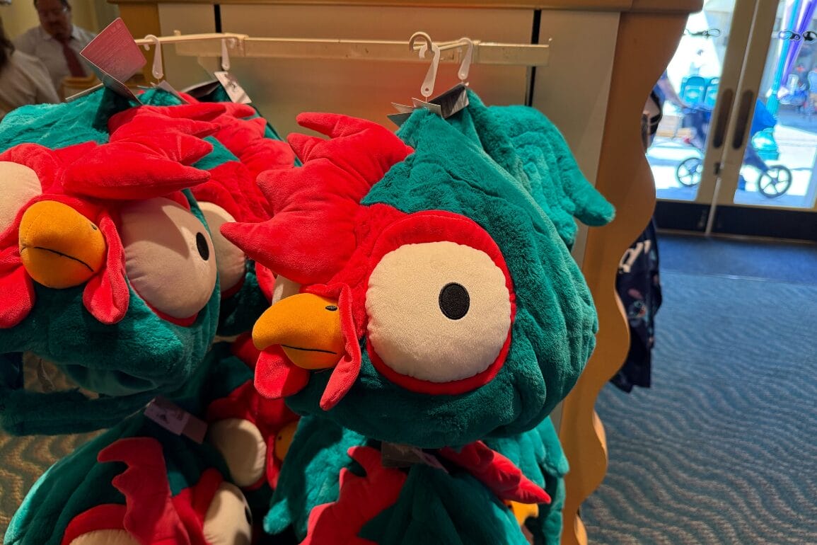 Plush hats shaped like colorful chickens with big eyes hang on a display rack in a store.