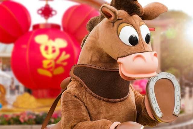Person in a brown horse costume with large eyes, in front of red lanterns with gold designs.