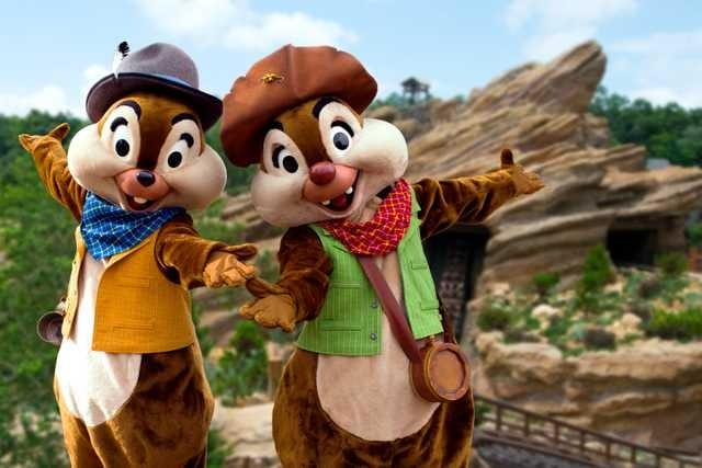 Two people in Chip and Dale costumes pose with arms outstretched outside in front of a rocky landscape.
