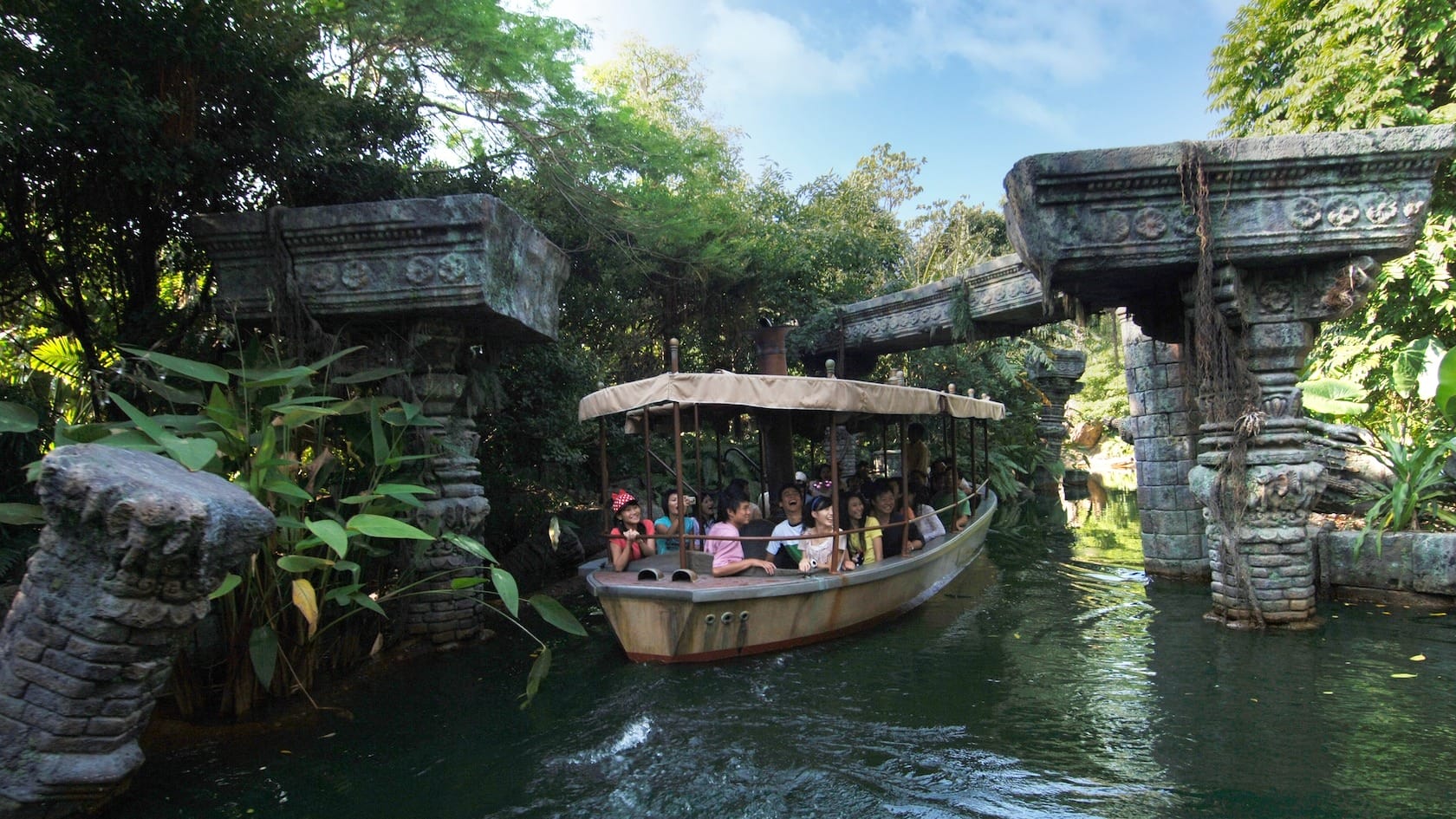A boat with people passes under ancient stone ruins on the Jungle Cruise Halloween at Hong Kong Disneyland.