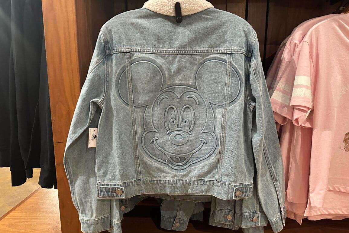 Light blue Mickey Denim Jacket with a large embossed Mickey Mouse face on the back, hanging on a clothing rack.